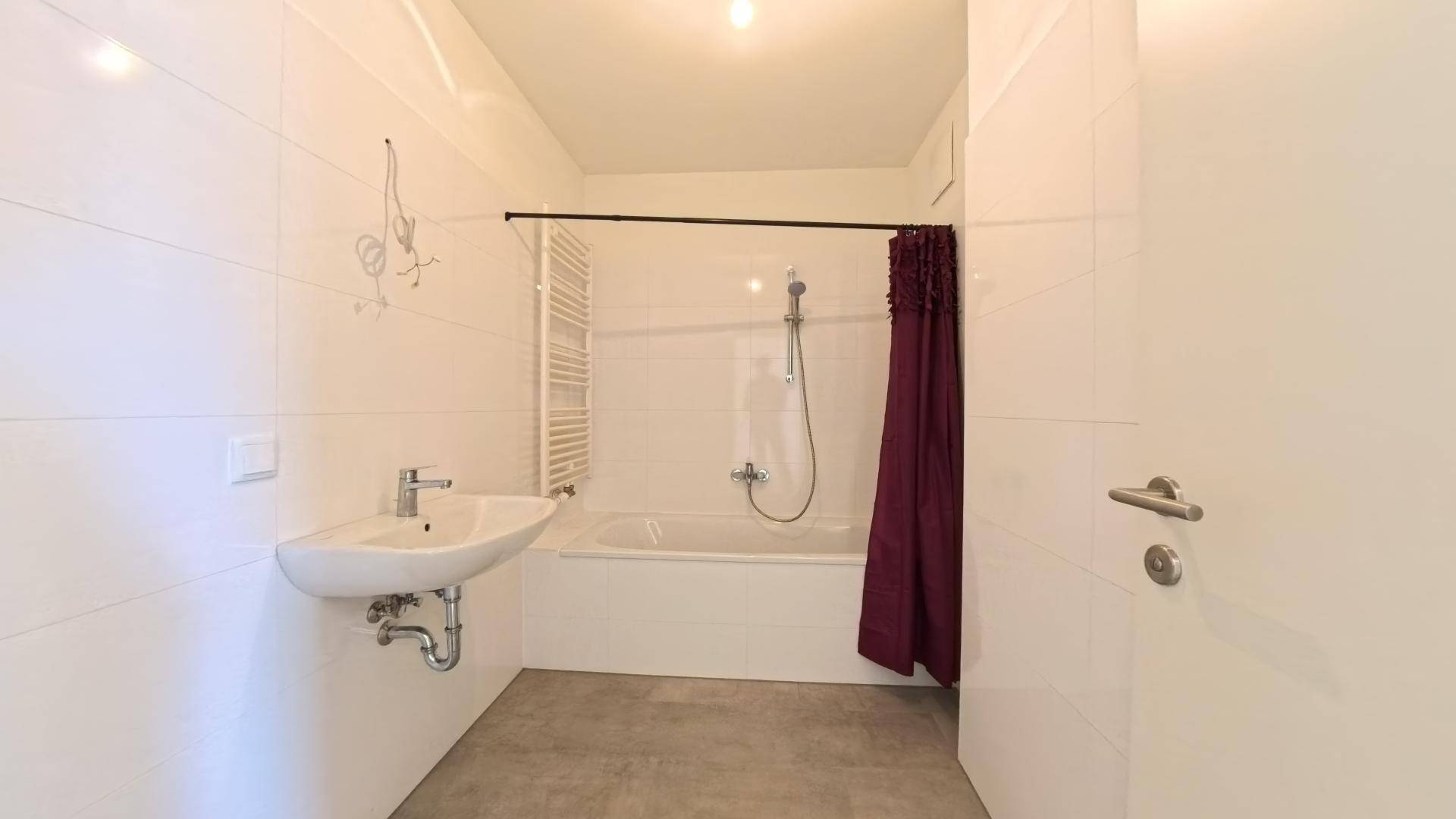 Modernes Badezimmer mit weißen Fliesen, Badewanne, Waschbecken und Handtuchheizkörper.