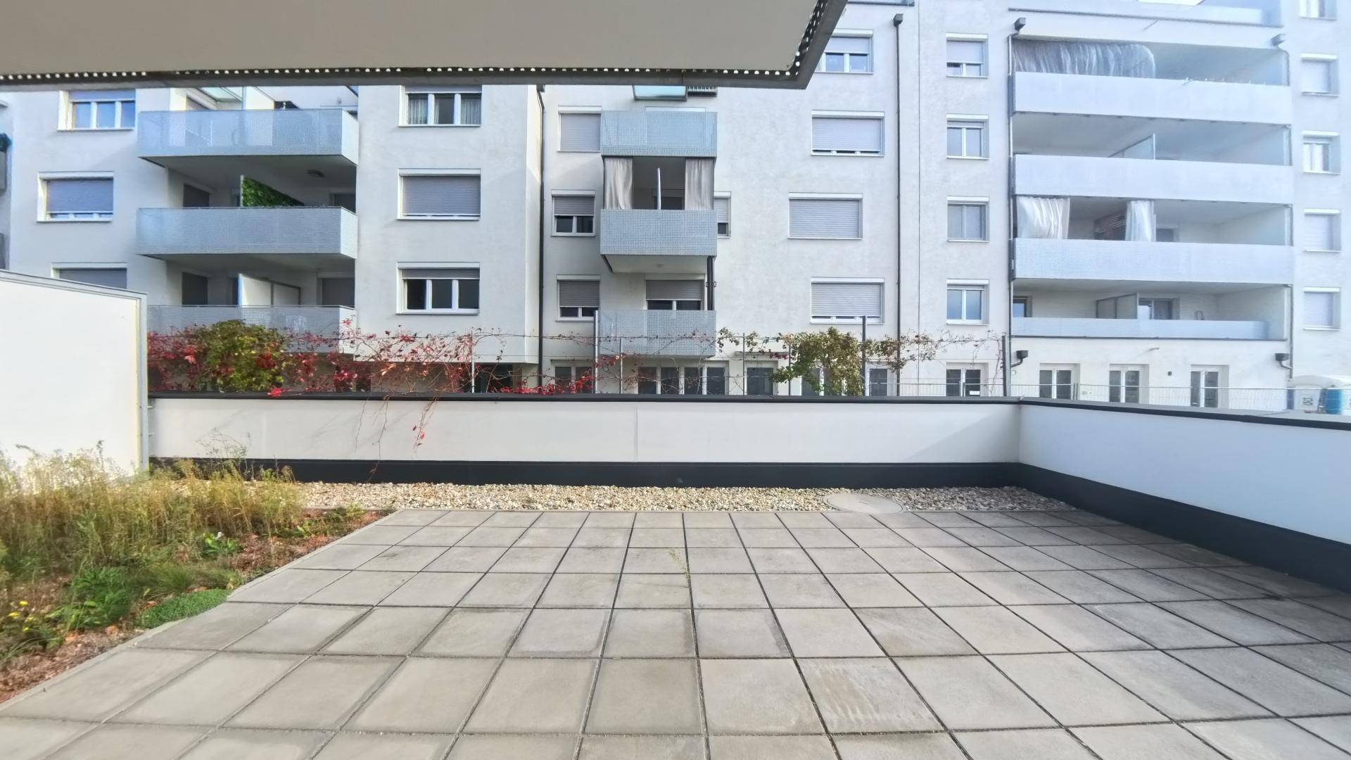 Große, geflieste Terrasse mit Kiesbeet und Blick auf die umliegenden Wohngebäude.