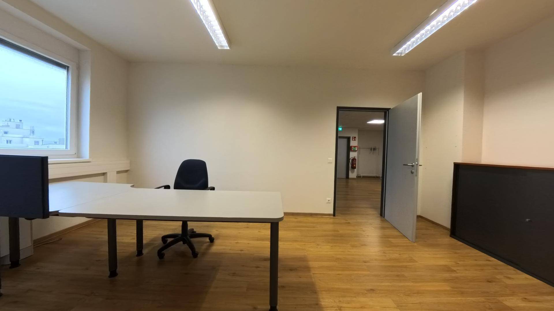 Büro mit Holzfußboden, Schreibtisch und offener Tür zu einem weiteren, hellen Raum.