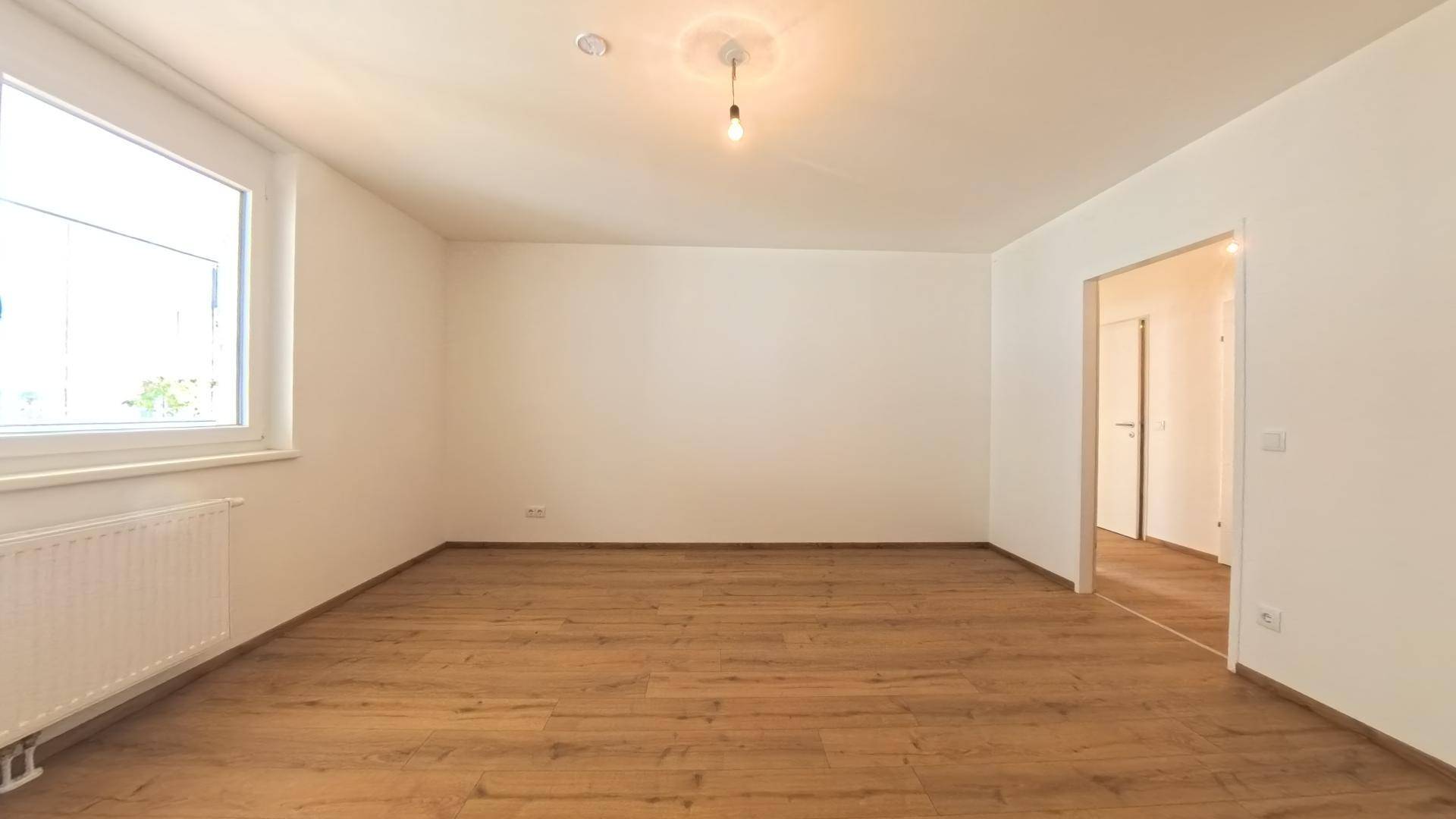 Geräumiges, helles Zimmer mit Laminatboden und einem großen Fenster.