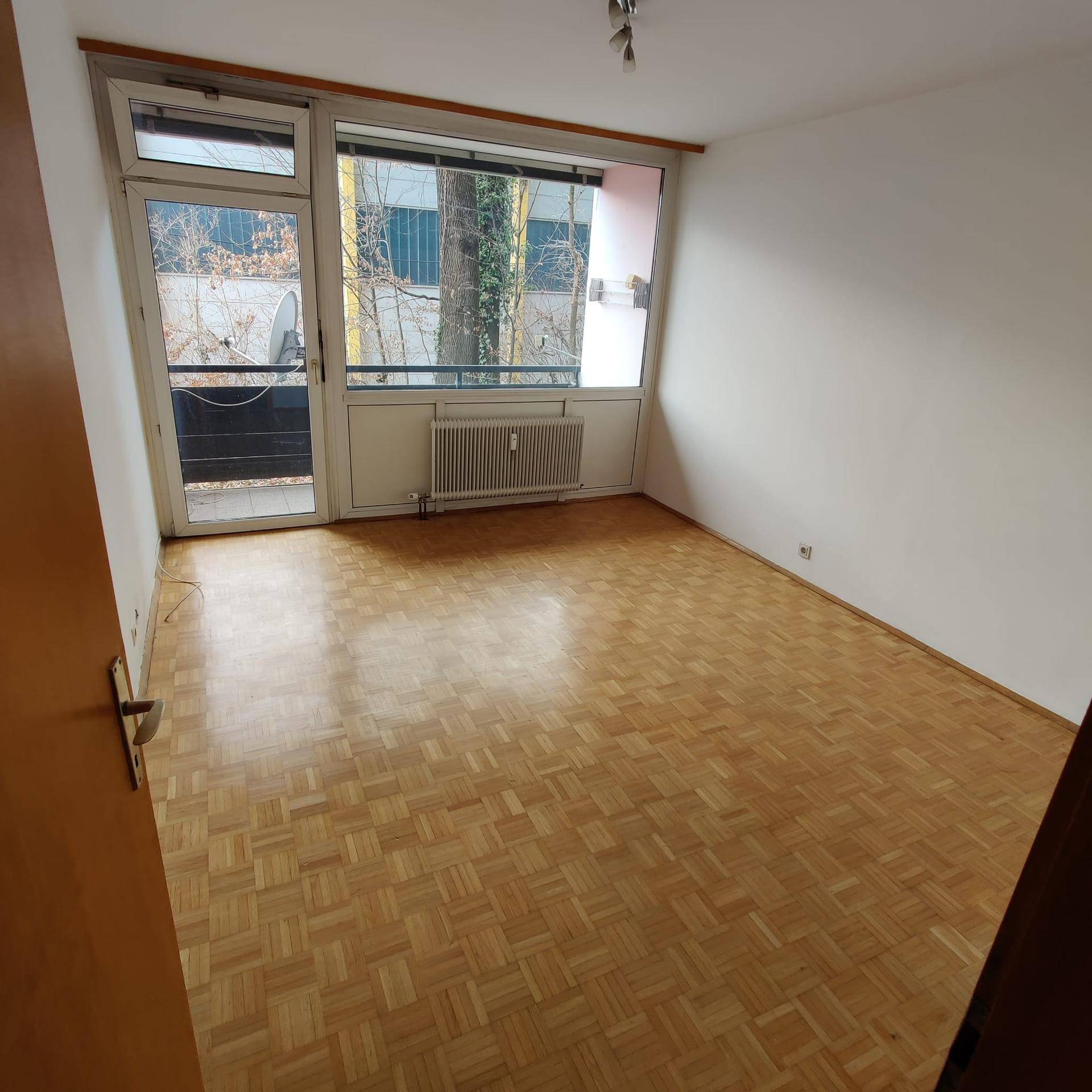 Geräumiges Zimmer mit Parkettboden, großem Fenster und Zugang zu einem Balkon.