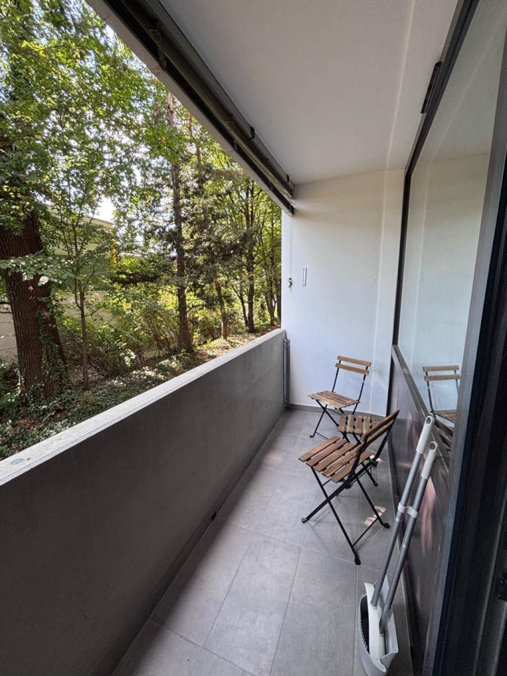 Balkon mit Blick ins Grüne, ausgestattet mit zwei Holzstühlen und einem kleinen Tisch.