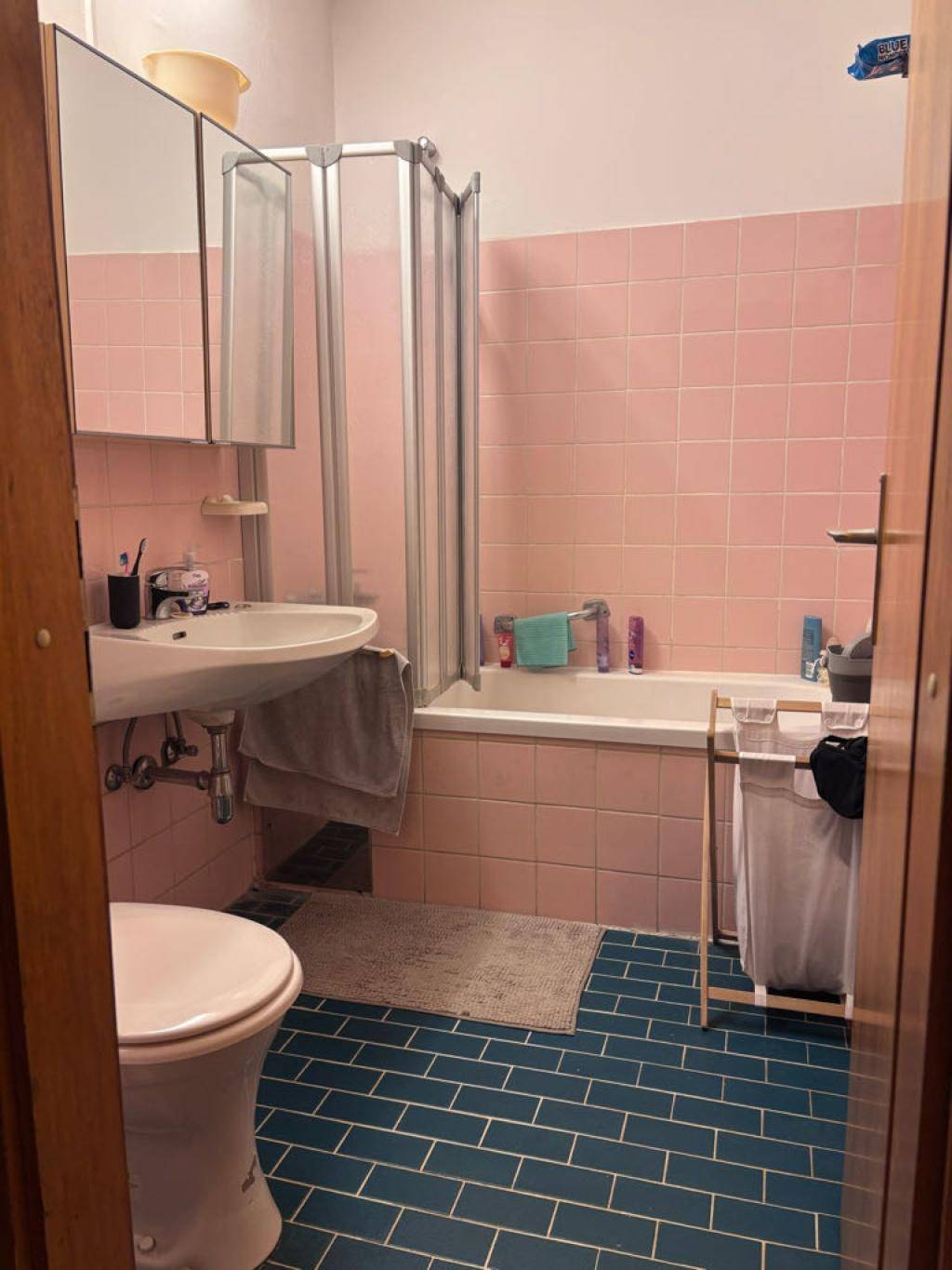 Badezimmer mit rosa Fliesen an den Wänden und blauen Fliesen auf dem Boden, inklusive Badewanne und Dusche.
