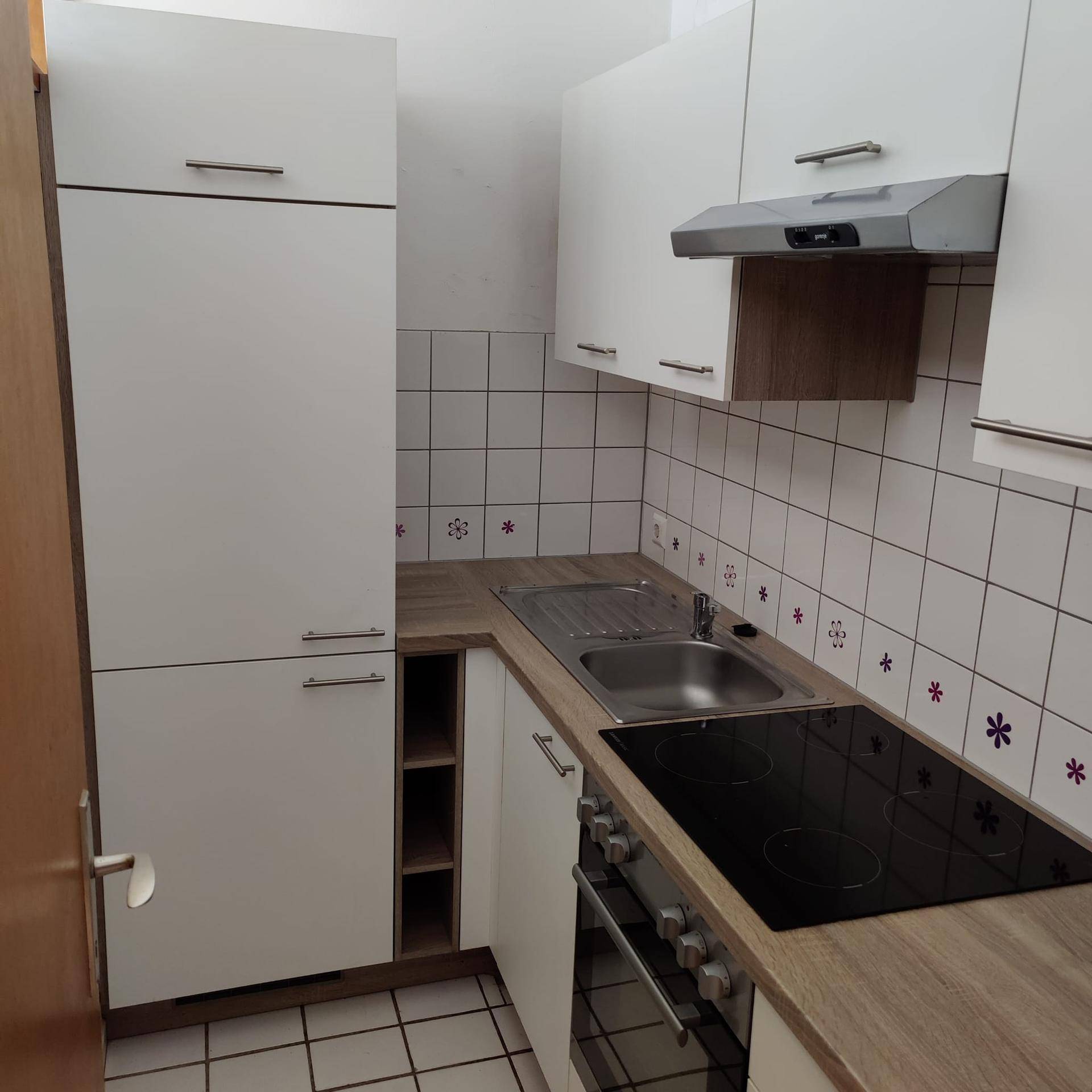 Kleine Küche mit weißen Schränken, Holzoptik-Arbeitsplatte und integrierten Geräten.