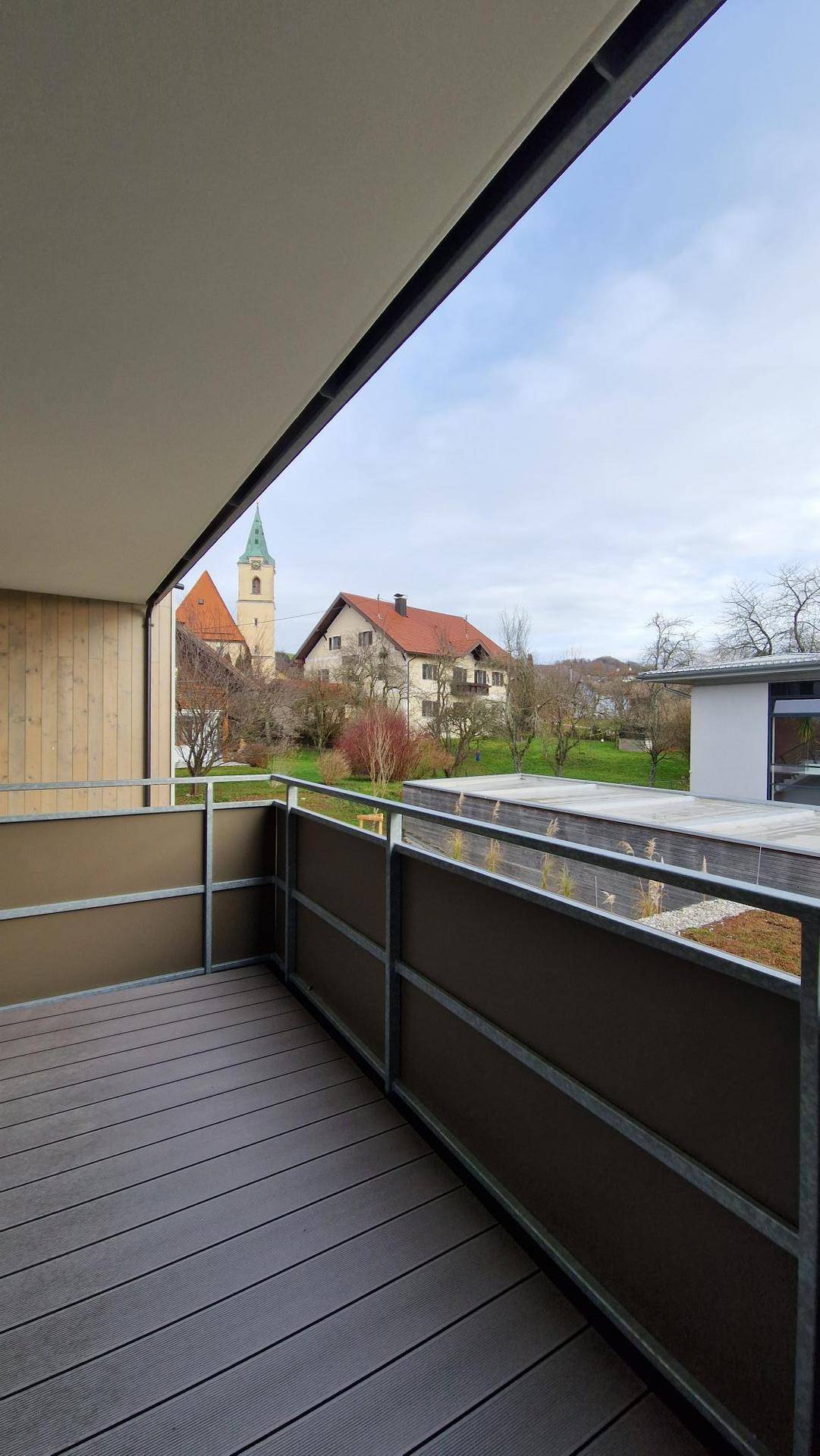 Balkon mit Holzdielenboden und Blick auf eine Kirche sowie die umliegende grüne Landschaft.