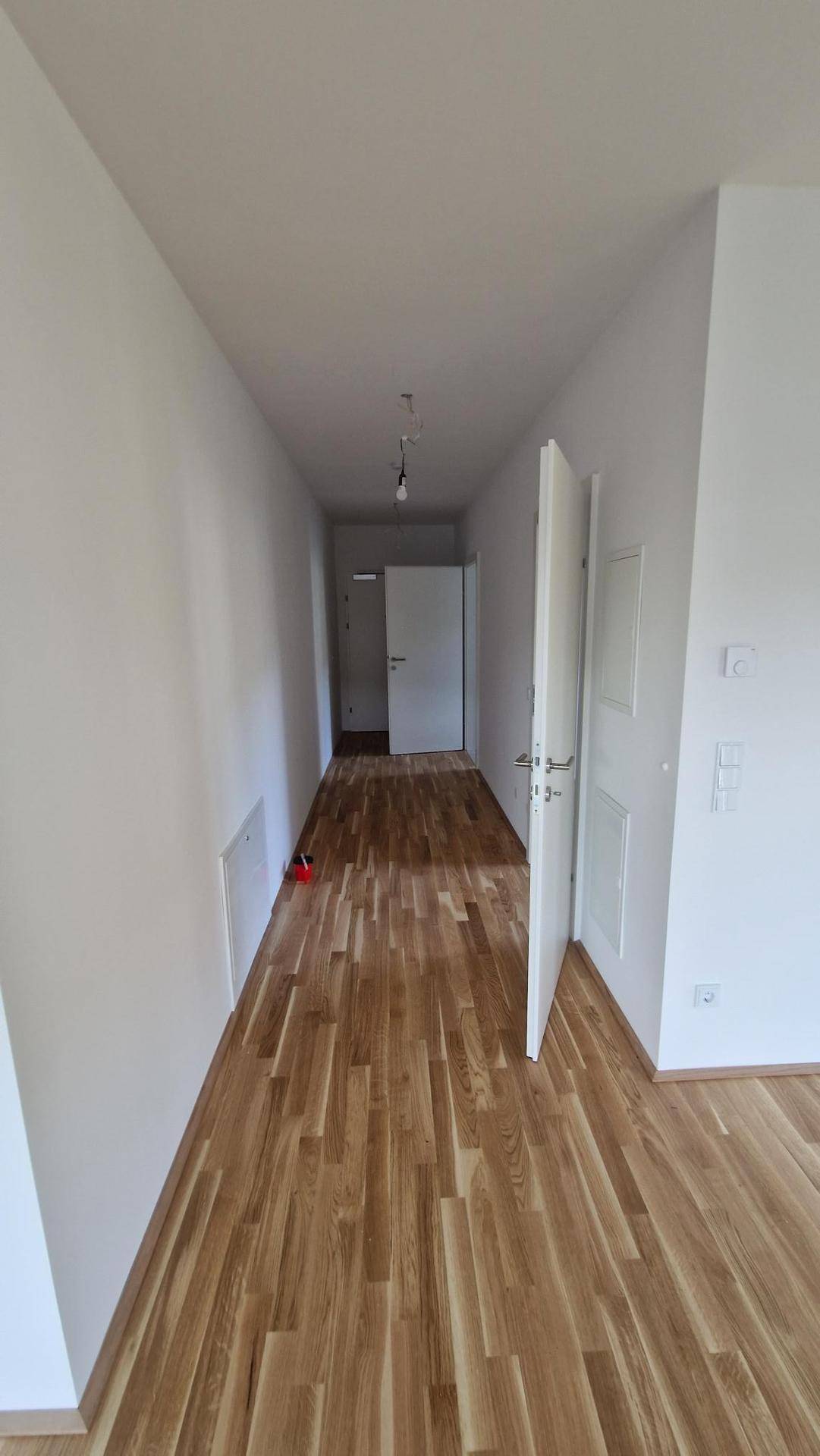 Langer Flur mit hellem Holzboden und weißen Türen, der verschiedene Räume verbindet.