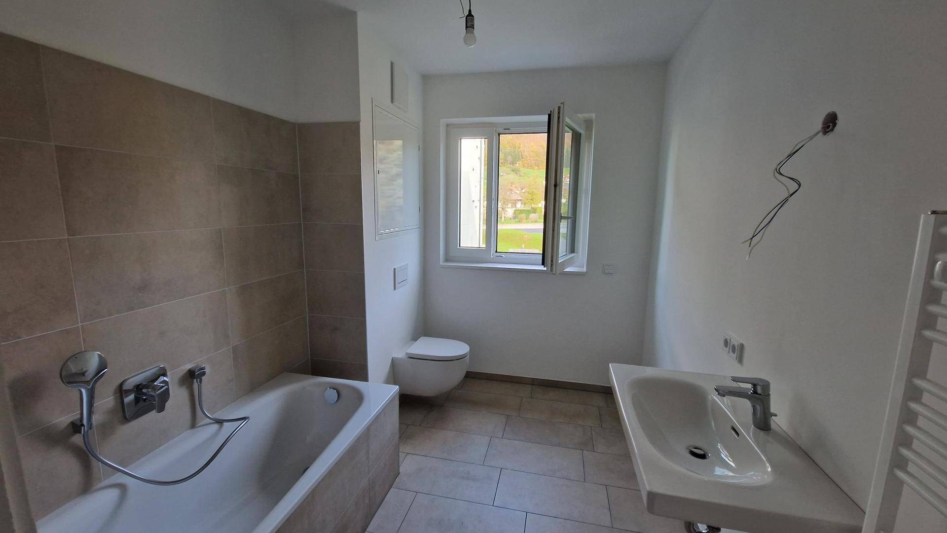 Modernes Badezimmer mit Badewanne, Einzelwaschbecken, Wand-WC und Fenster für Tageslicht.