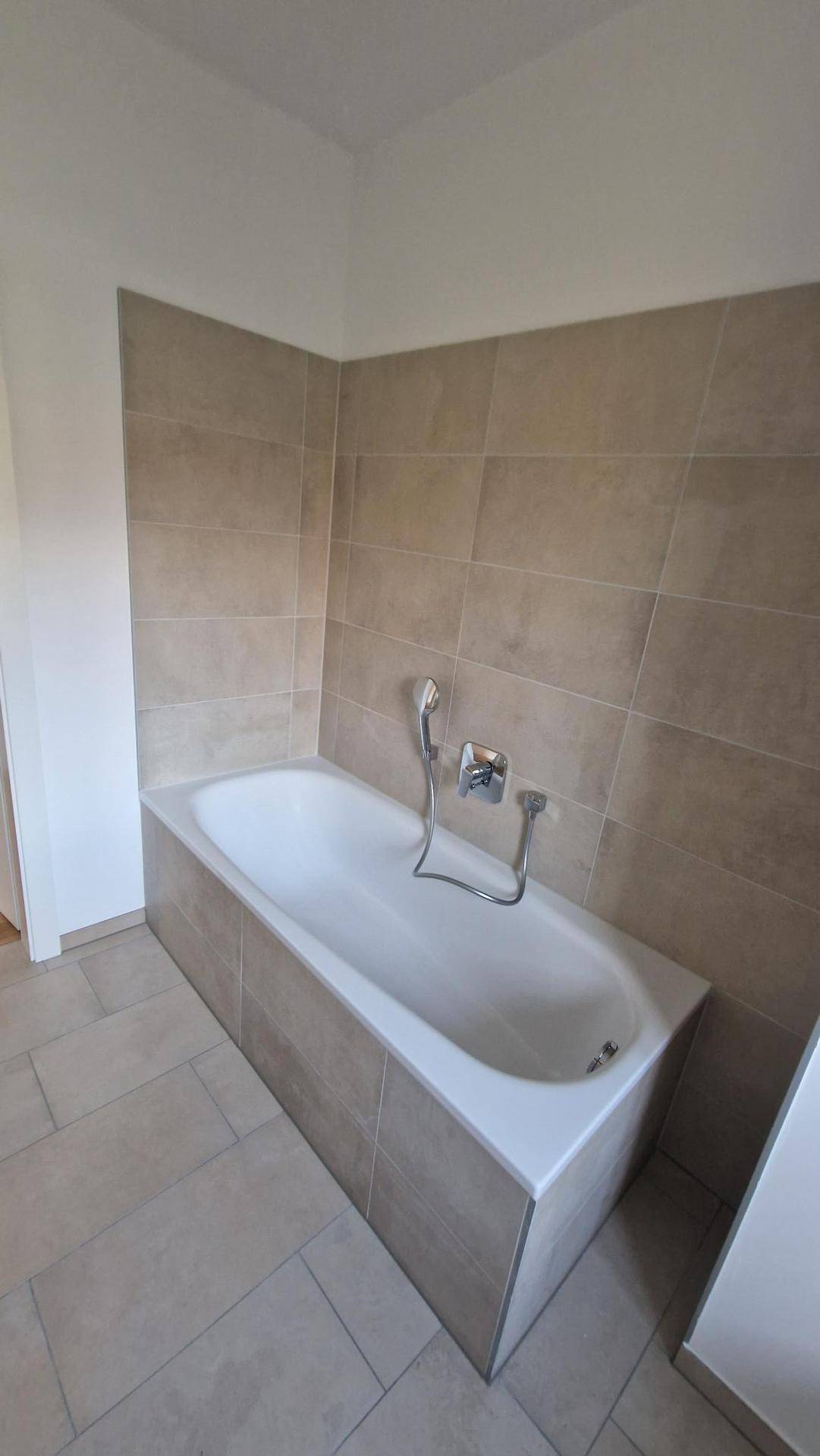 Eingebaute Badewanne mit beigefarbenen Fliesen und moderner Armatur in einem Badezimmer.