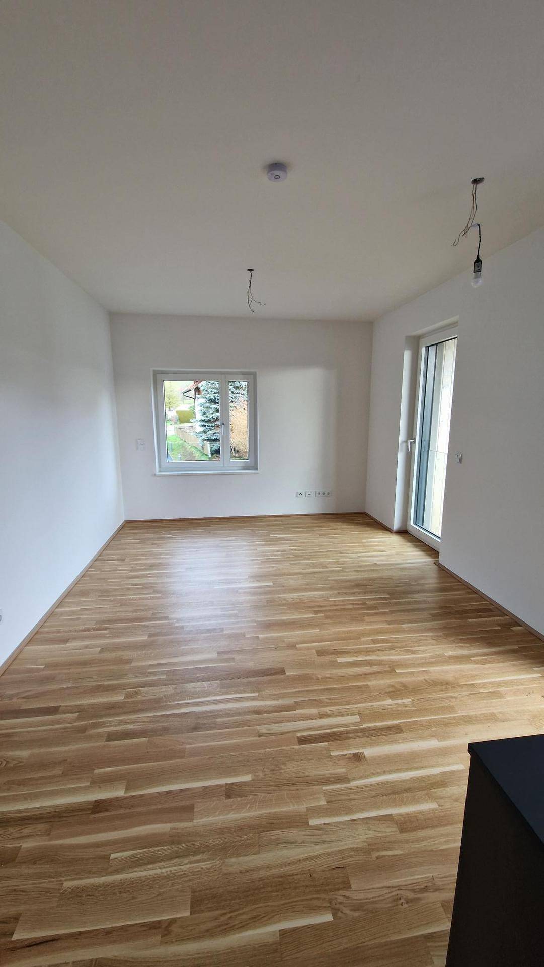 Helles Zimmer mit Holzboden und Fenster, das einen grünen Ausblick bietet, ideal als Schlafzimmer.