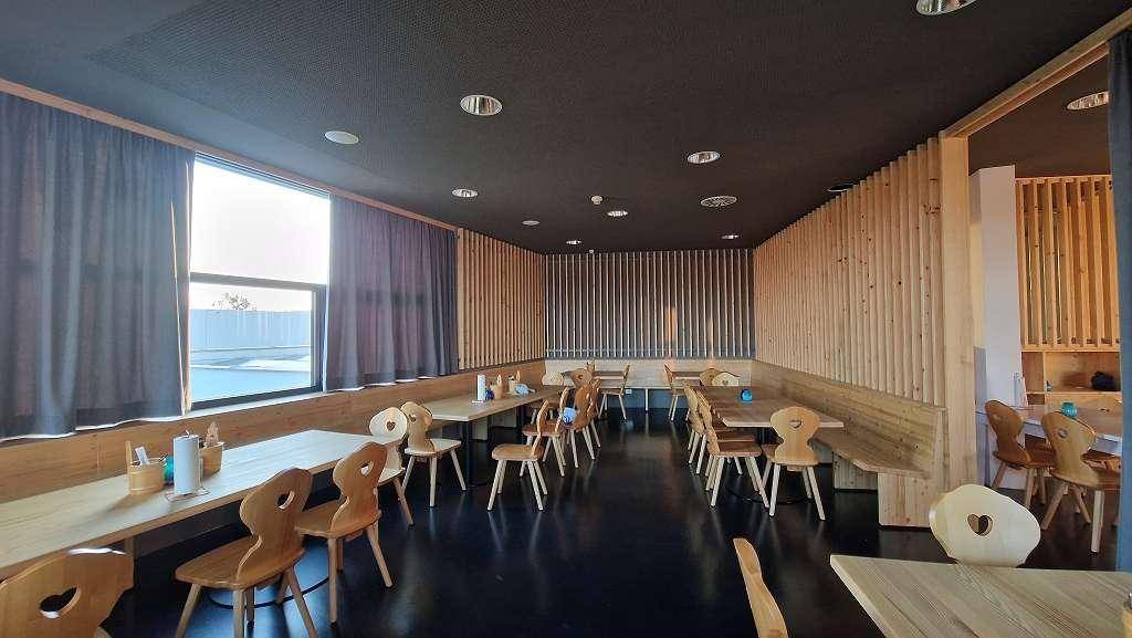 Gemütlicher Restaurantbereich mit Holztischen und -stühlen, dunklen Vorhängen und Holzvertäfelungen.