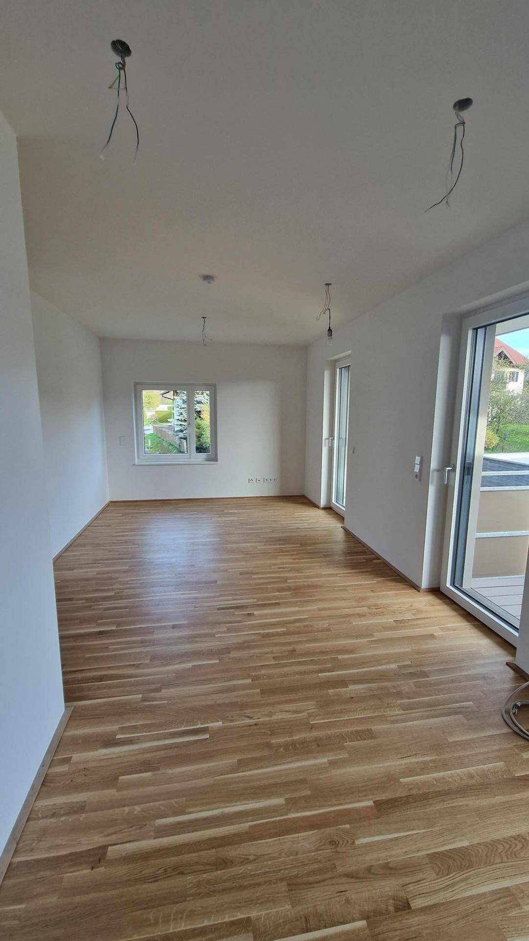 Geräumiger, heller Raum mit Holzboden und großen Fenstern, bereit für individuelle Gestaltung.