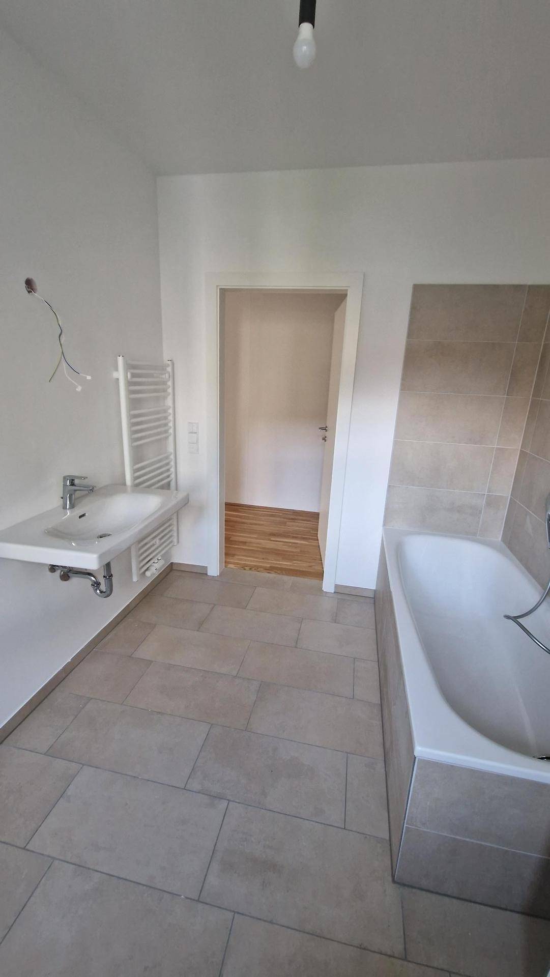 Badezimmer mit Badewanne, Einzelwaschbecken und beheiztem Handtuchhalter, ausgestattet mit Fliesenboden.