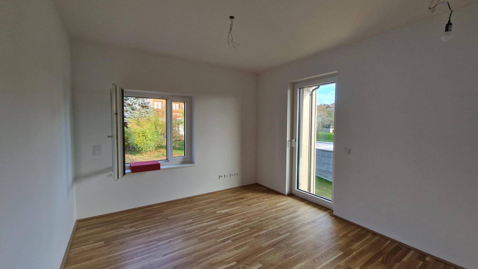 Helles Zimmer mit Holzboden, großem Fenster und Zugang zu einem Balkon, ideal als Schlafzimmer.