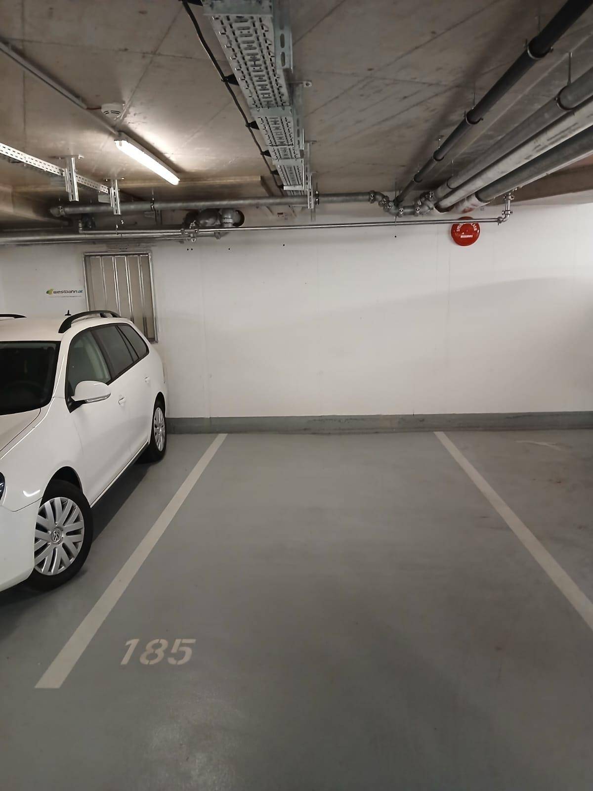 Heller Tiefgaragenstellplatz mit Betonwänden und sichtbaren Installationen an der Decke, gut beleuchtet.