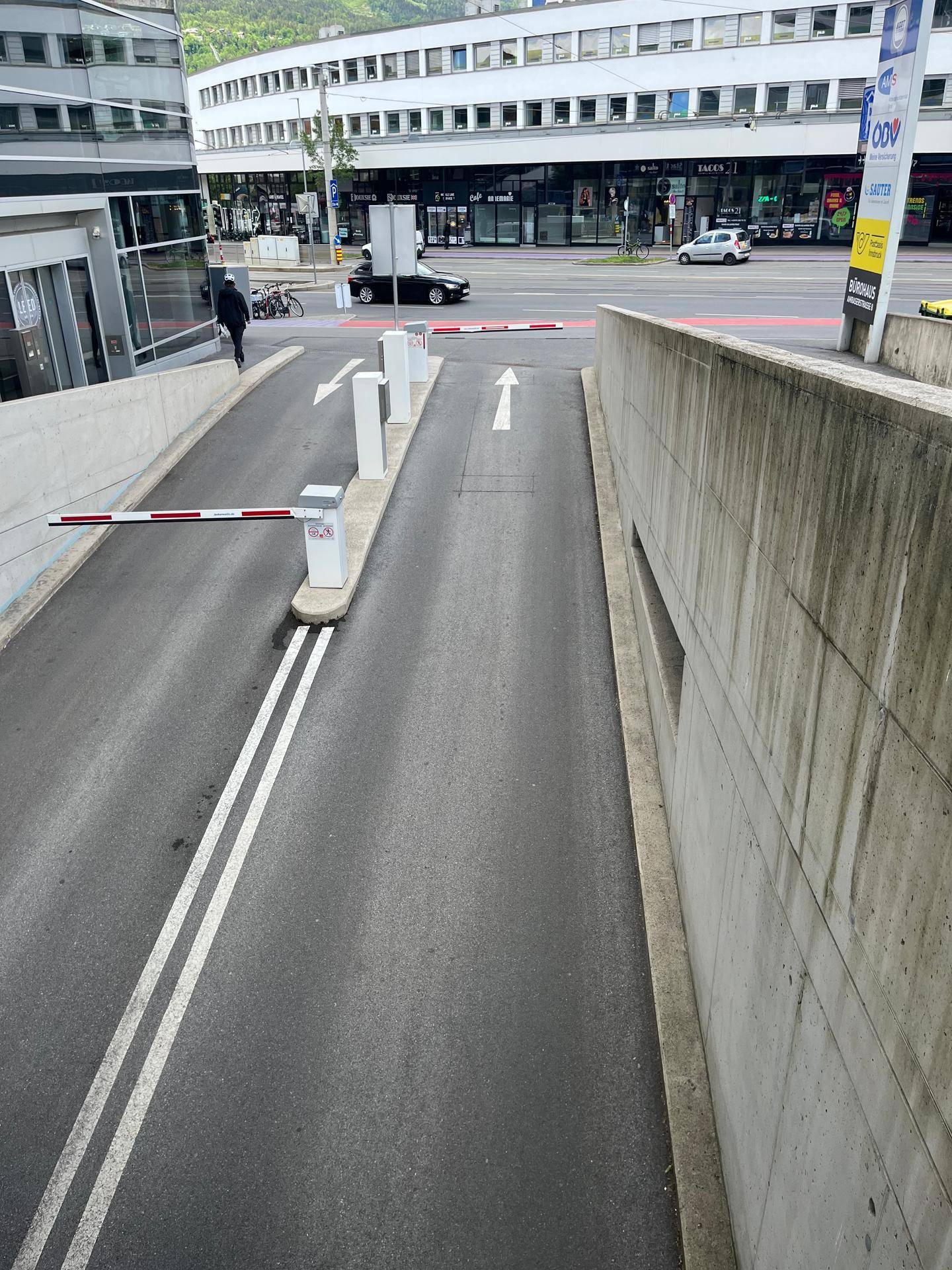 Ausfahrt der Tiefgarage mit Schranke und Blick auf die belebte Straße und umliegende Stadtgebäude.