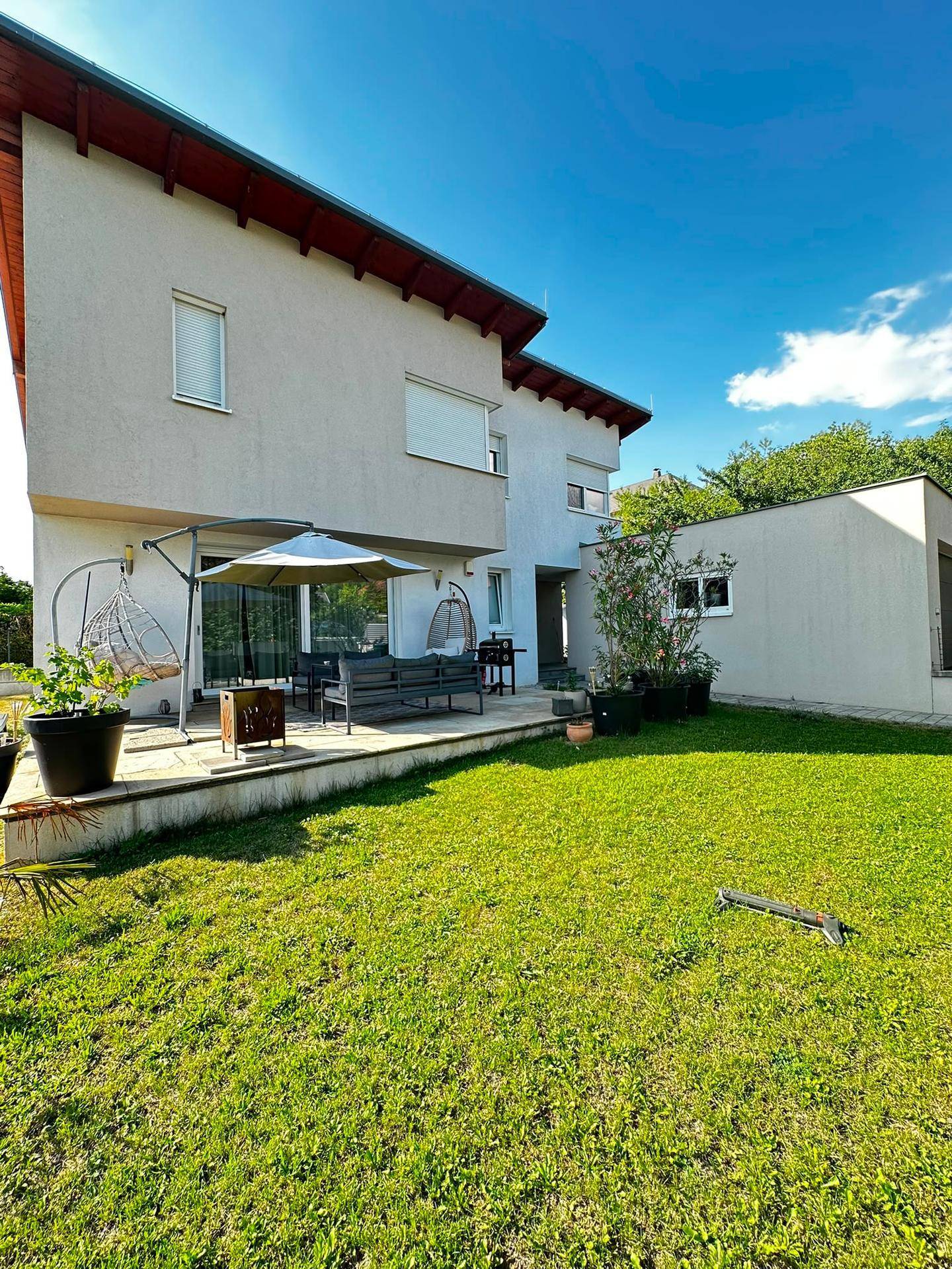 Sonniger Garten mit Rasenfläche, Terrasse und modernen Gartenmöbeln.