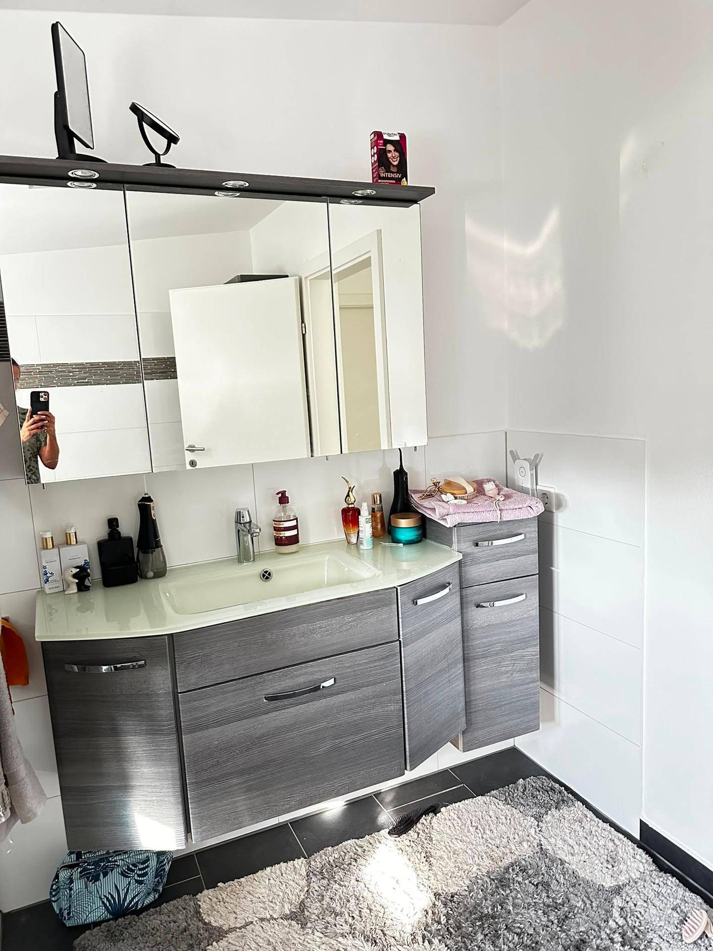 Badezimmer mit modernem Waschtischunterschrank, Spiegelschrank und dunklen Bodenfliesen.