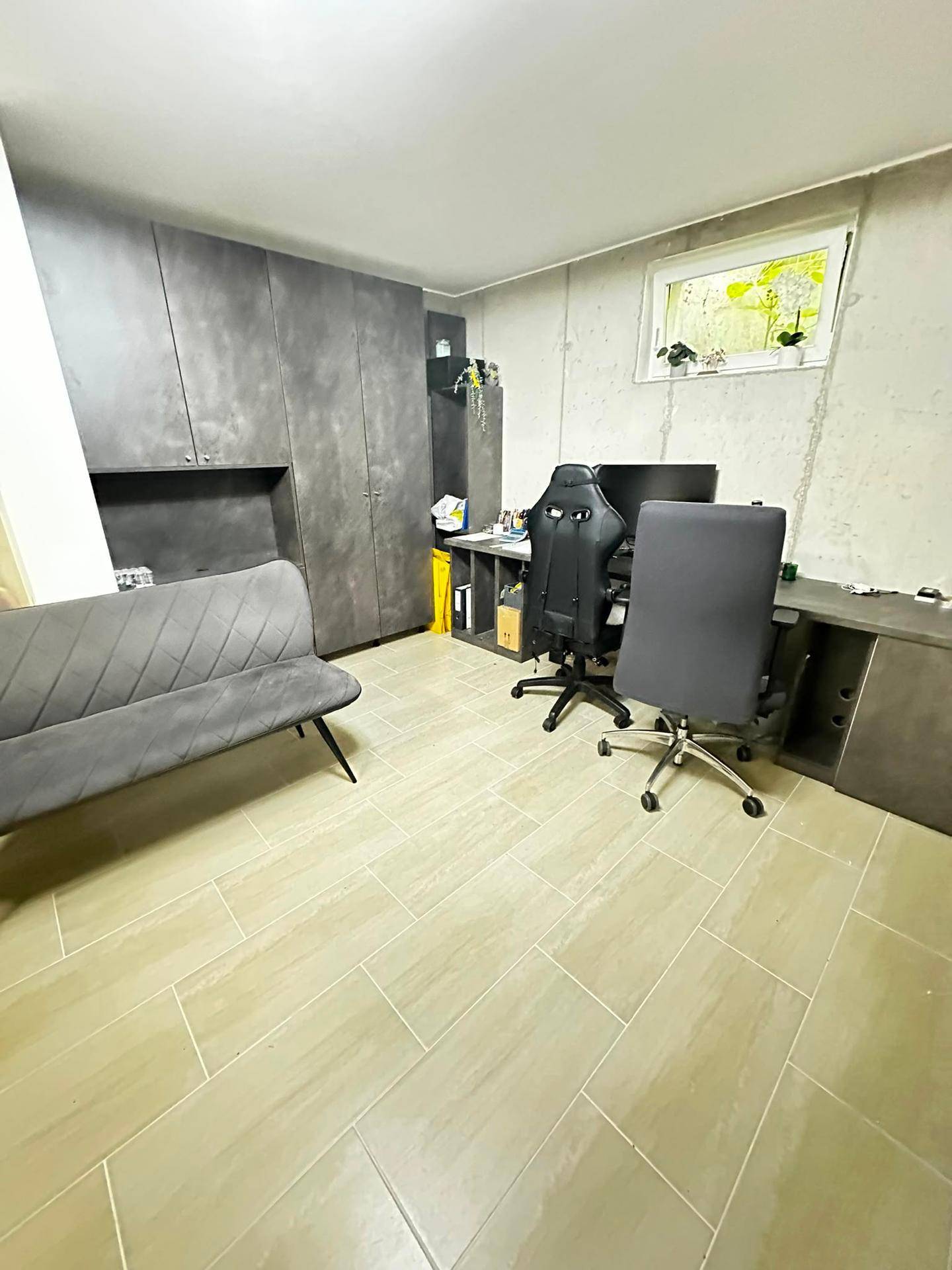 Modernes Heimbüro mit grauen Schränken, Schreibtisch und hellen Fliesen.