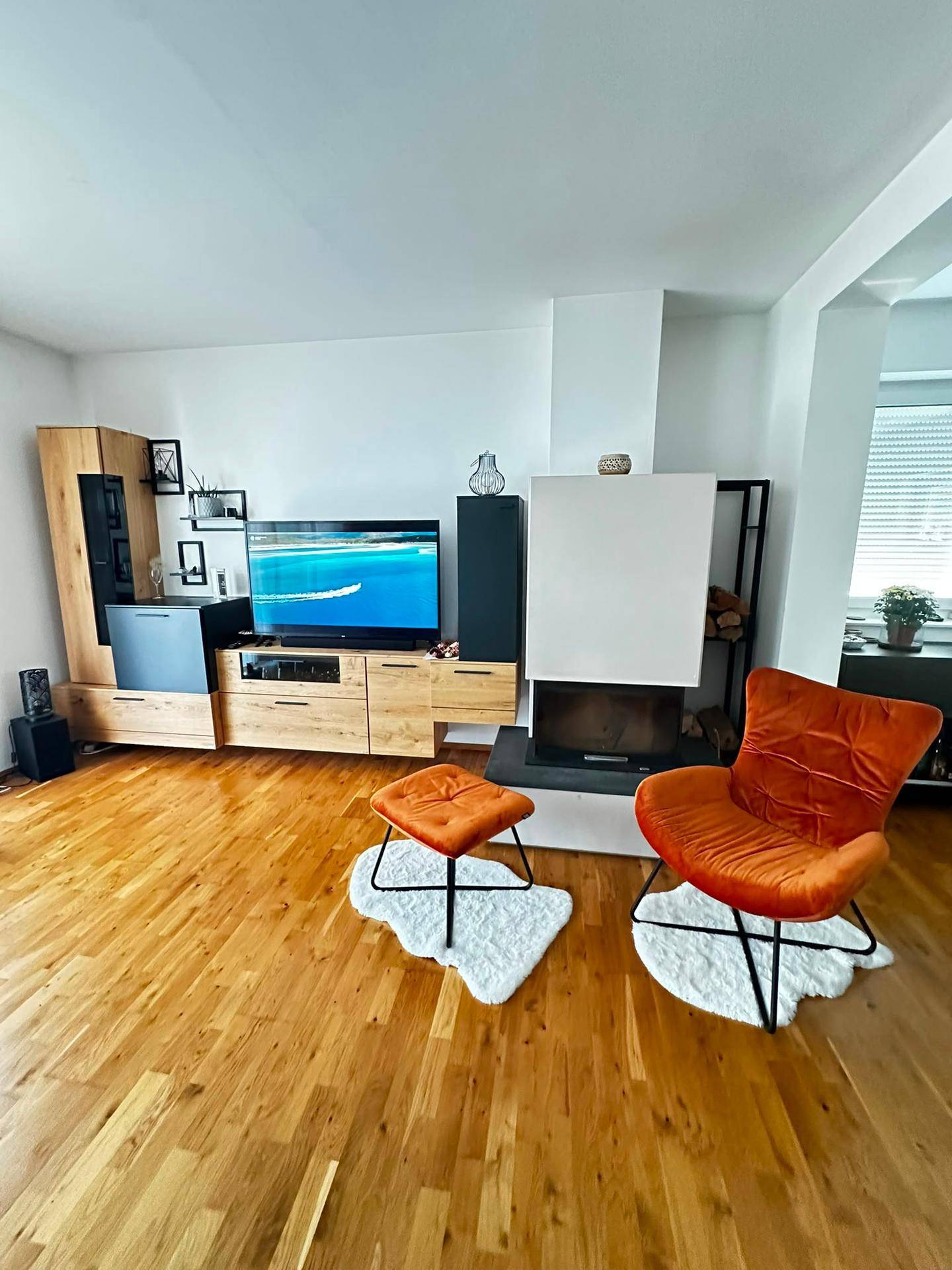 Helles Wohnzimmer mit Holzboden, Kamin und modernen Möbeln in warmen Farben.
