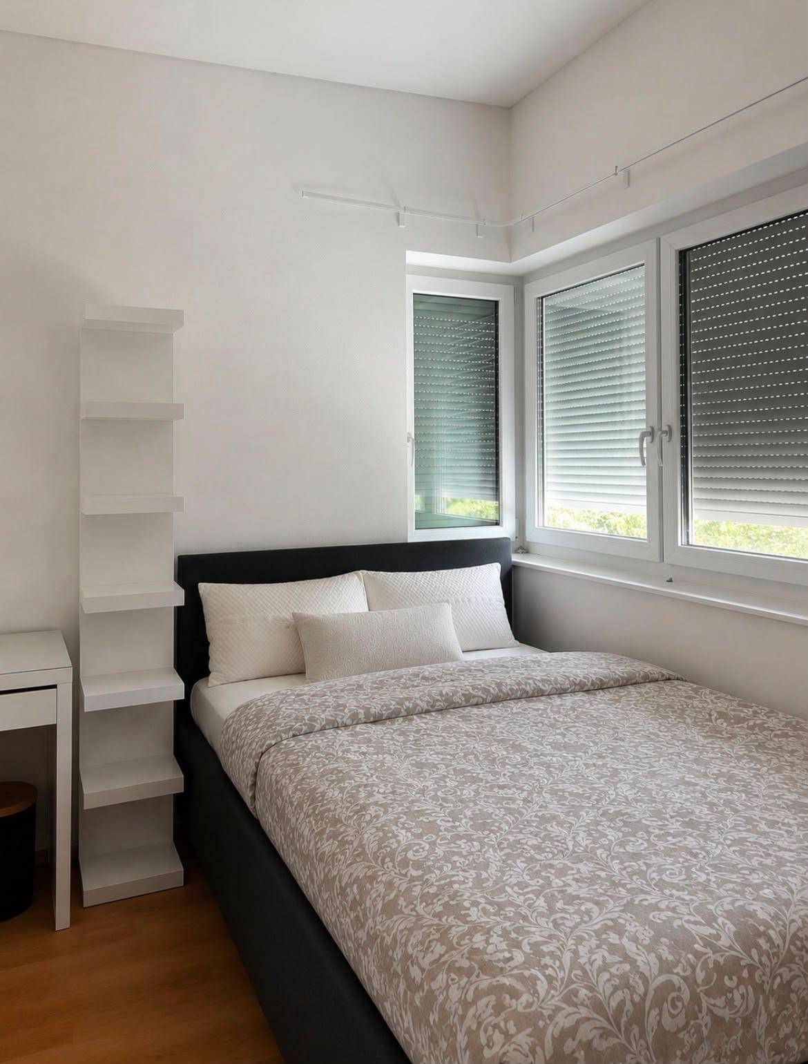Helles Schlafzimmer mit Doppelbett, Holzboden und großen Fenstern.