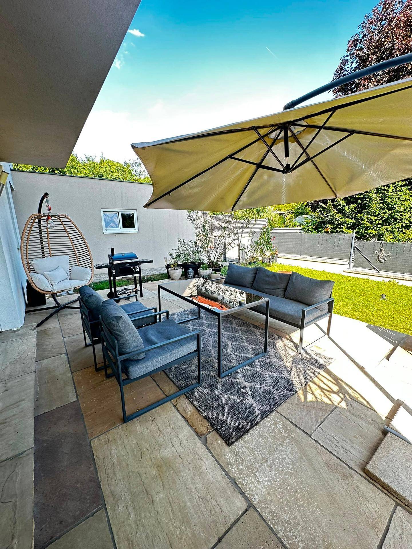 Gemütliche Terrasse mit Sitzgruppe, großem Sonnenschirm und Steinplattenboden.