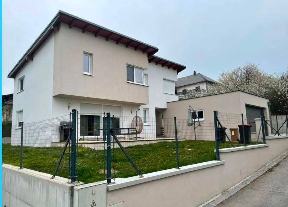 Modernes Einfamilienhaus mit Garten, Terrasse und Zaun in grüner Umgebung.