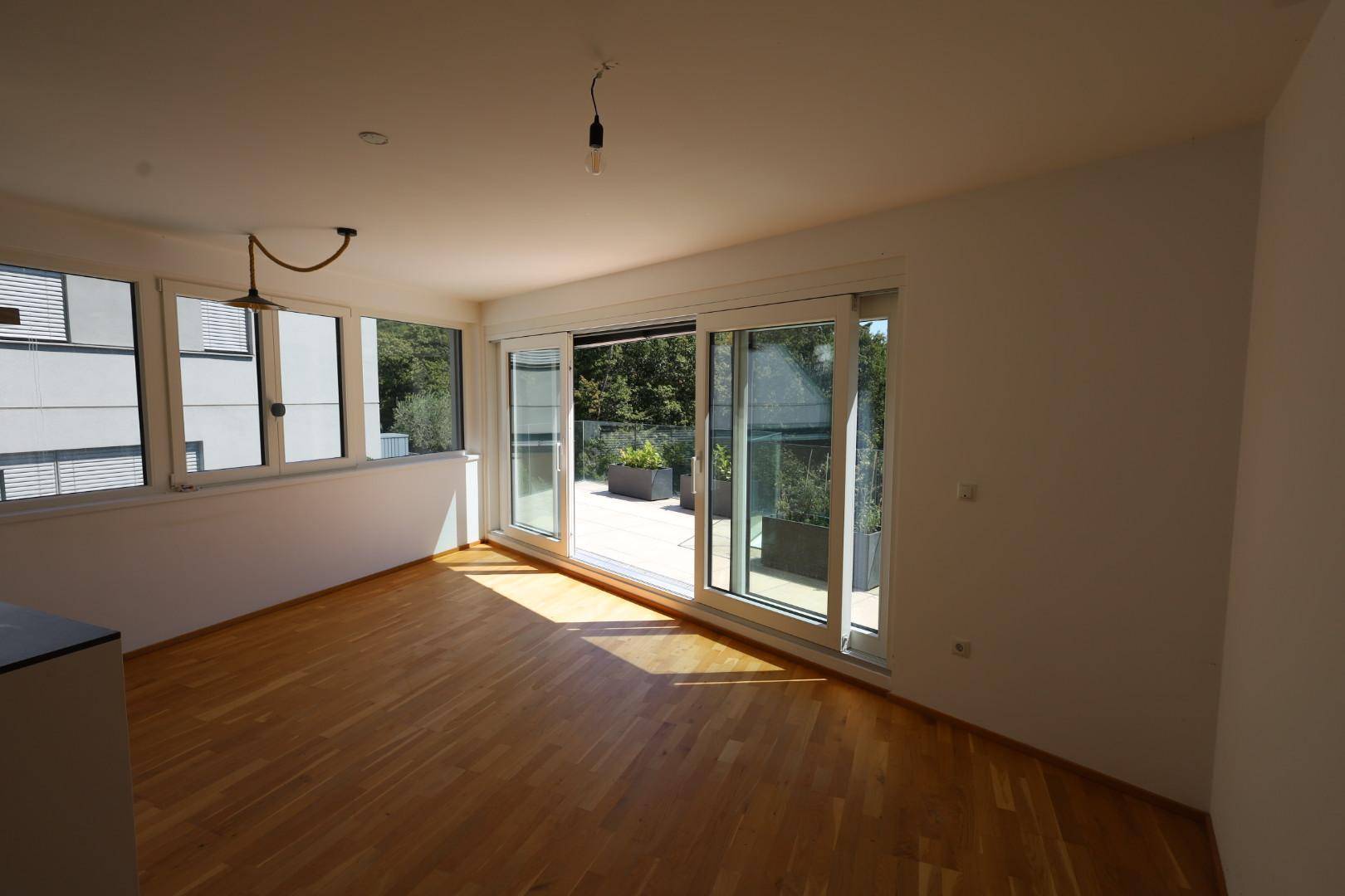 Geräumiger Wohnbereich mit hellem Holzboden und weitem Blick durch die großen Terrassentüren.