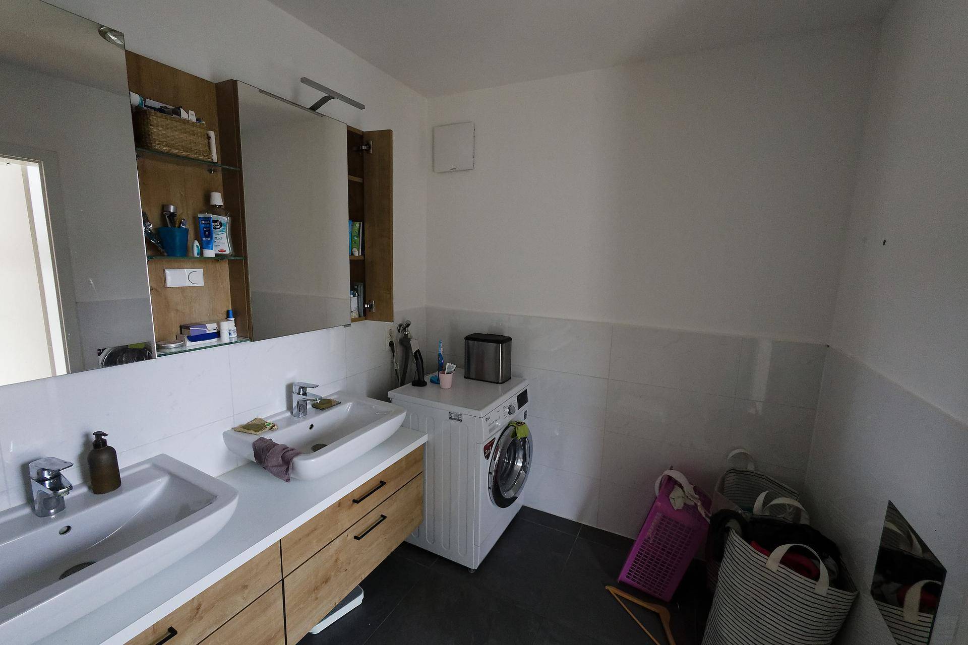 Badezimmer mit Doppelwaschbecken, Spiegelschrank und Platz für eine Waschmaschine.