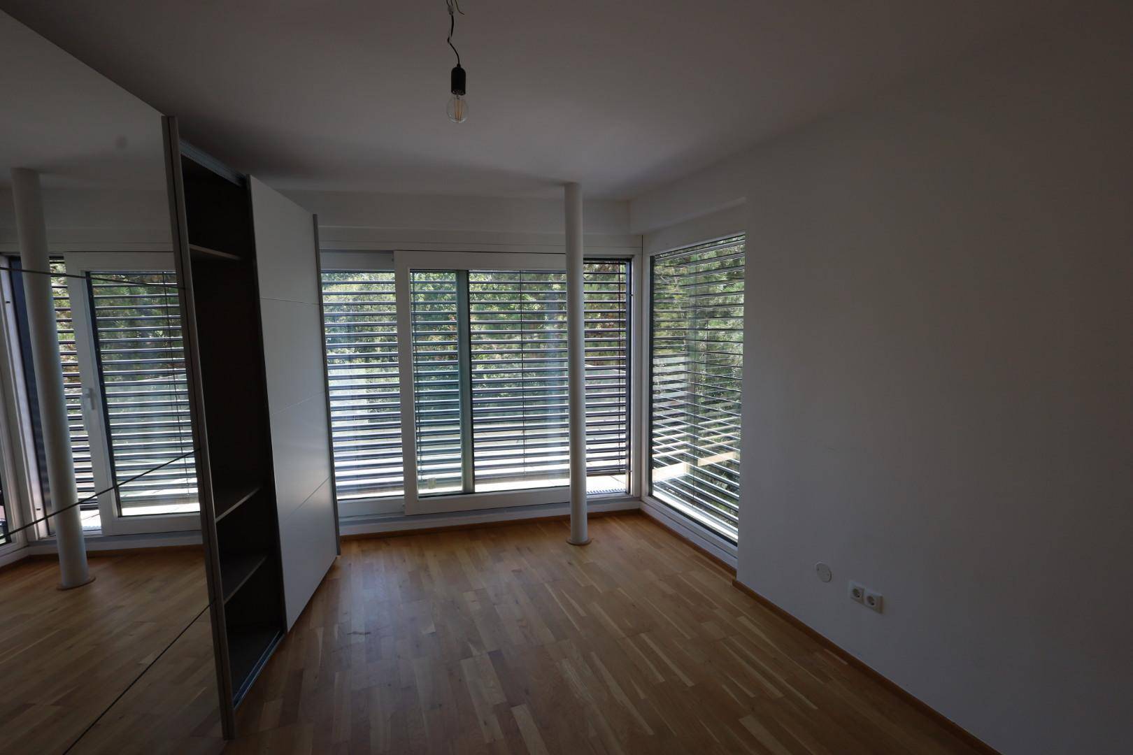 Helles Schlafzimmer mit Holzboden, großen Fenstern und integriertem Kleiderschrank.