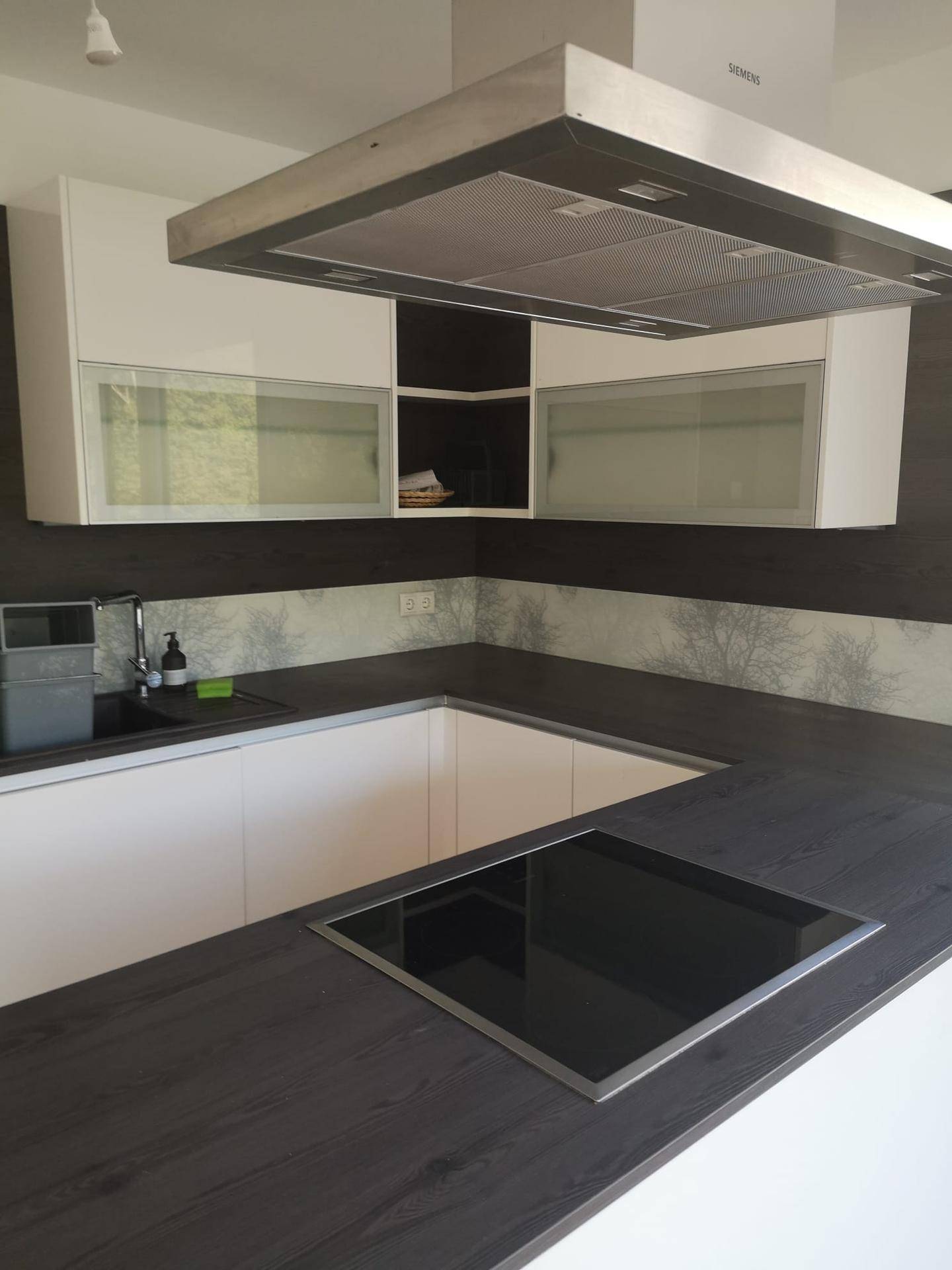 Moderne Einbauküche mit dunklen Arbeitsplatten, weißen Schränken und Induktionskochfeld.