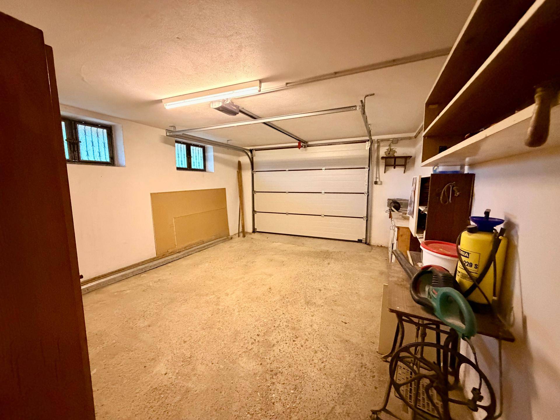 Geräumige Garage mit Rolltor, Betonboden und Stauraum, bietet Platz für Fahrzeuge und Lagerung.