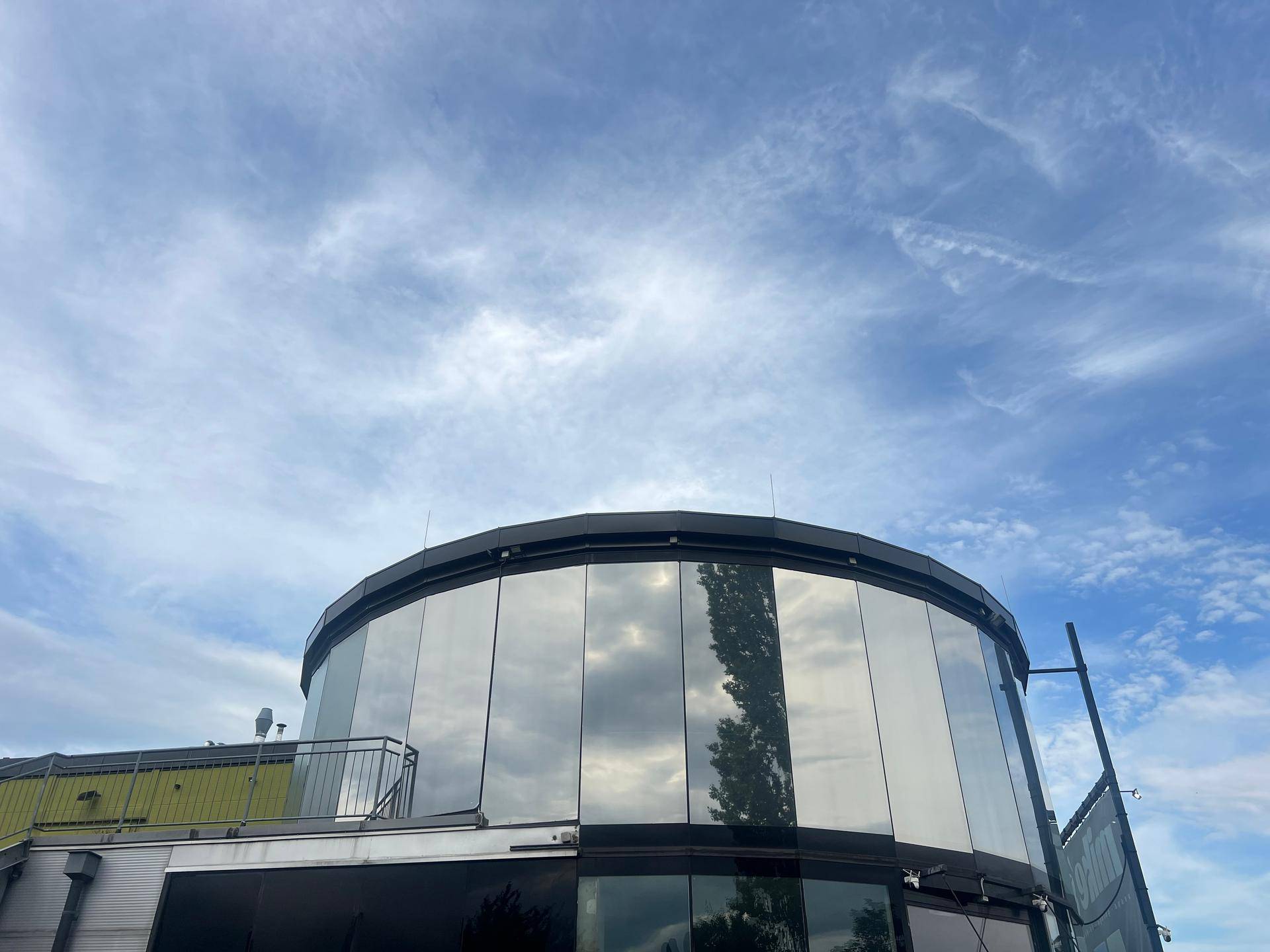 Nahaufnahme der runden Glasfassade des modernen Gebäudes, die den Himmel widerspiegelt.
