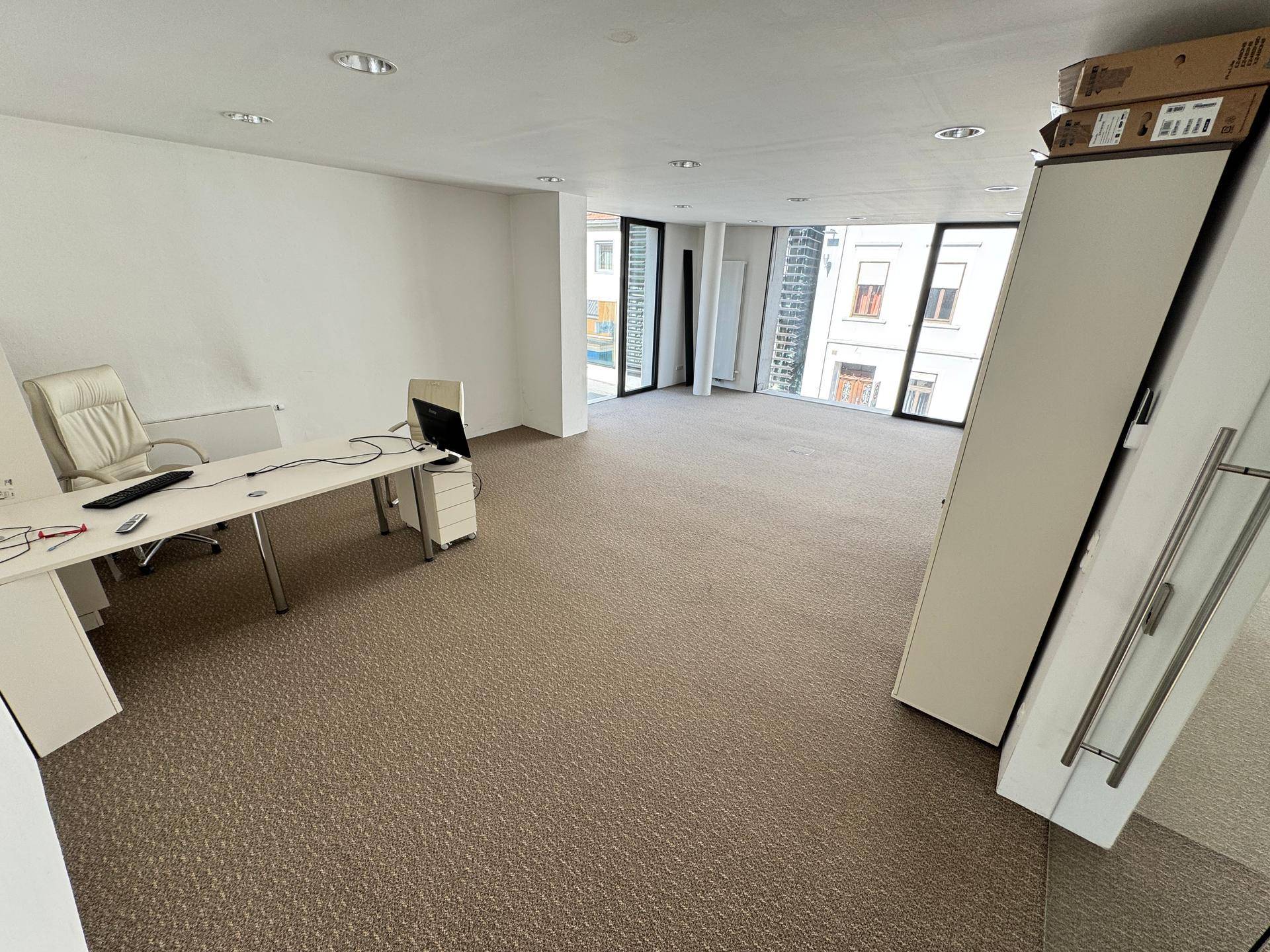 Helles Büro mit Teppichboden, großen Fenstern und moderner Einrichtung, bereit zur Nutzung und gut beleuchtet.