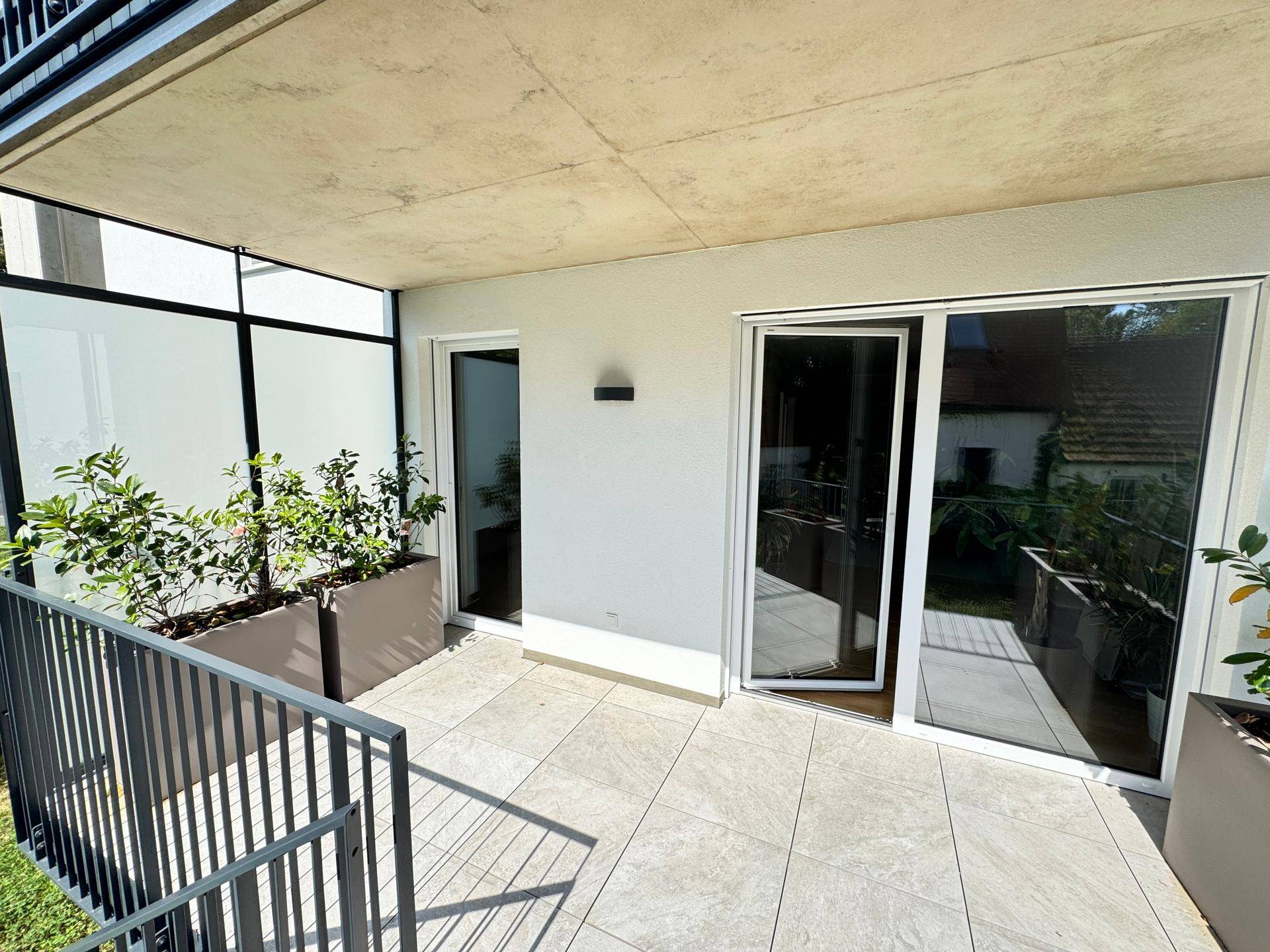 Geflieste Terrasse mit Pflanzen in Kübeln und Zugang zum Gartenbereich, ideal zum Entspannen.