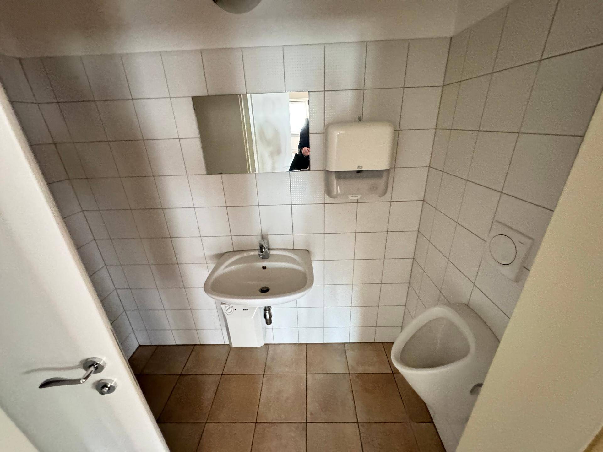 Badezimmer mit Urinal, Einzelwaschbecken und weißen Fliesen an den Wänden.