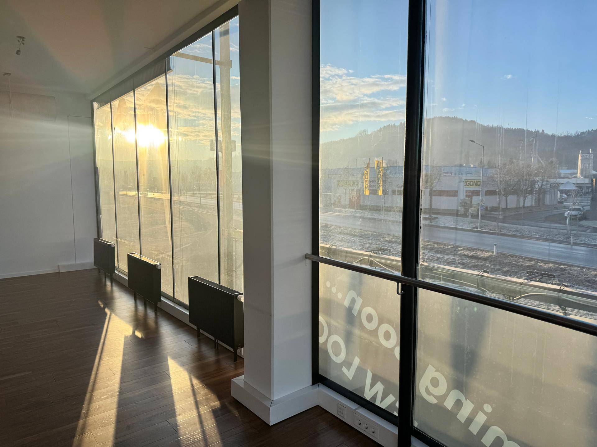 Gebogene Fensterfront mit Blick auf die Stadt und die umliegenden Berge, die viel Sonnenlicht hereinlässt.