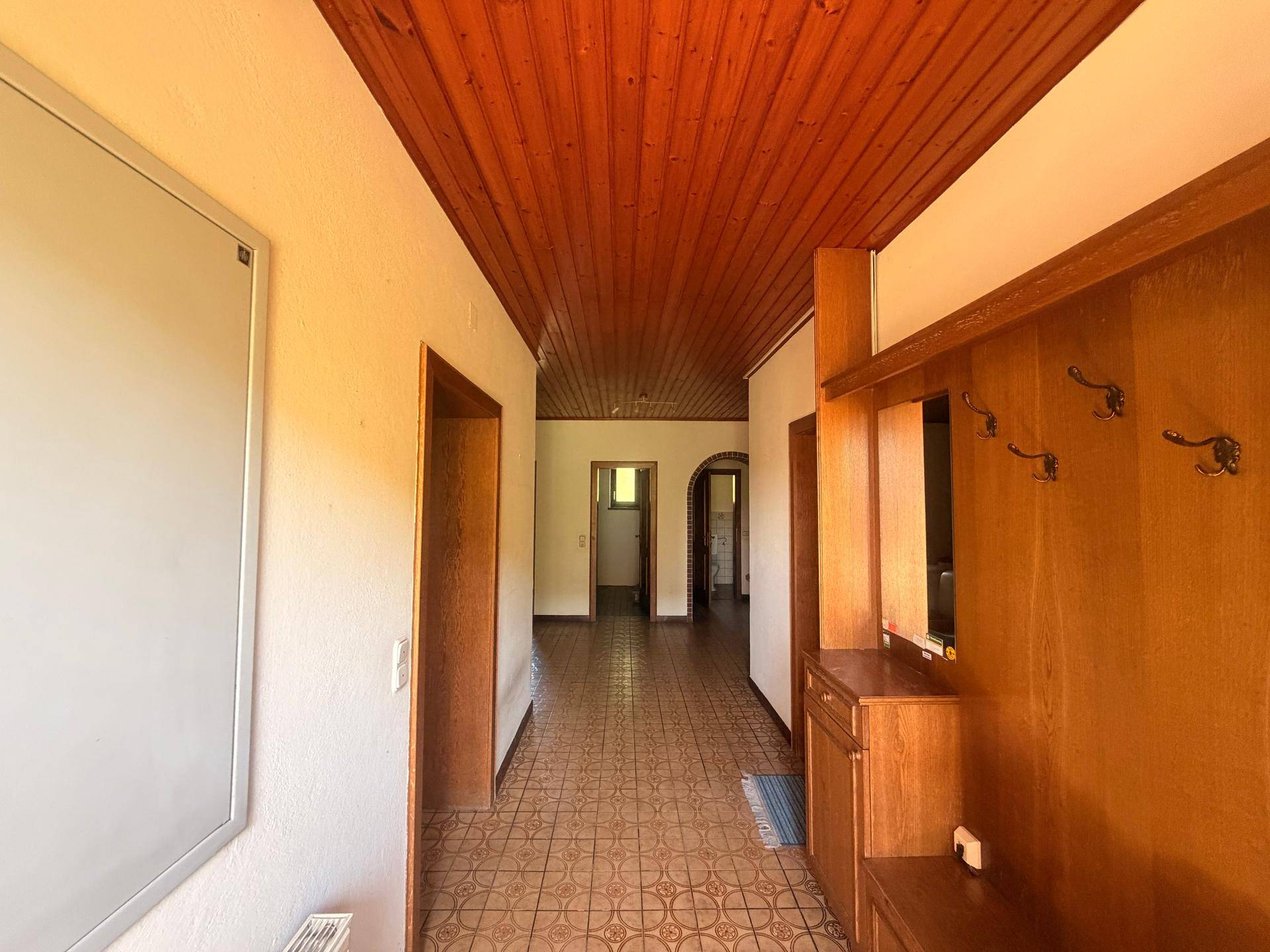 Langer Flur mit Holzdecke, gefliestem Boden und traditioneller Garderobe.