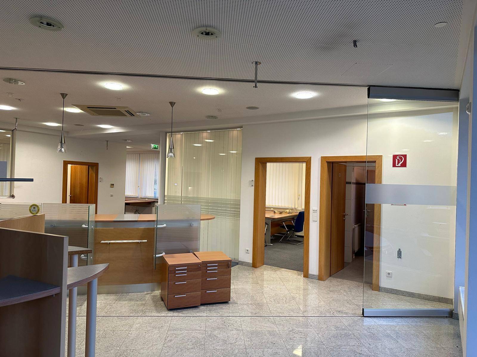 Offener Bürobereich mit Schaltern, Glaswänden und Zugang zu weiteren Räumen.