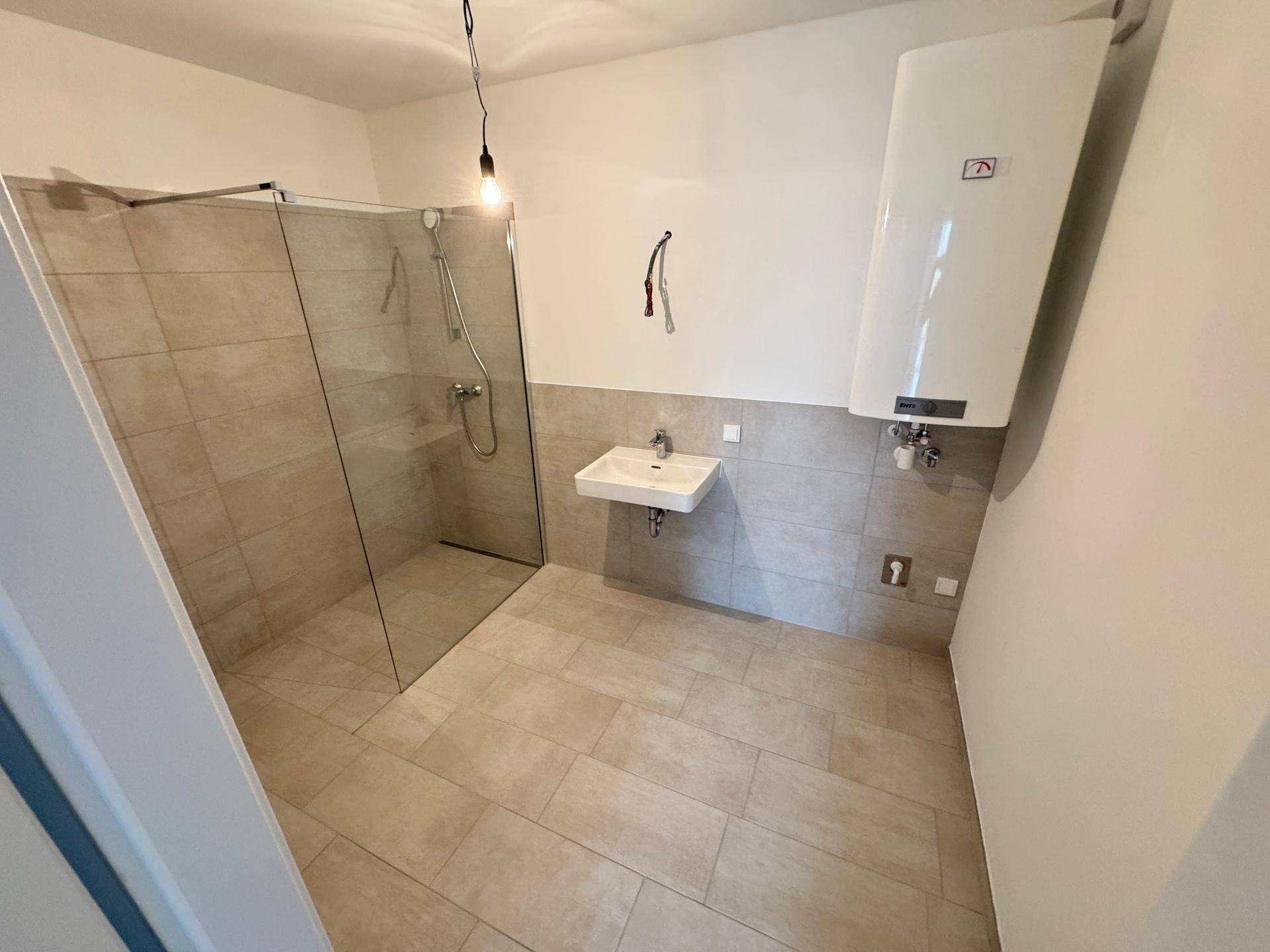 Modernes Badezimmer mit ebenerdiger Glasdusche, Waschbecken und hellen Fliesen an Wänden und Boden.