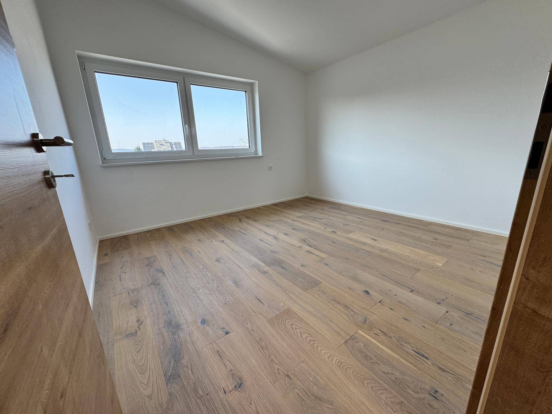 Schlafzimmer mit Holzboden, weiß gestrichenen Wänden und einem Fenster mit weitem Ausblick.