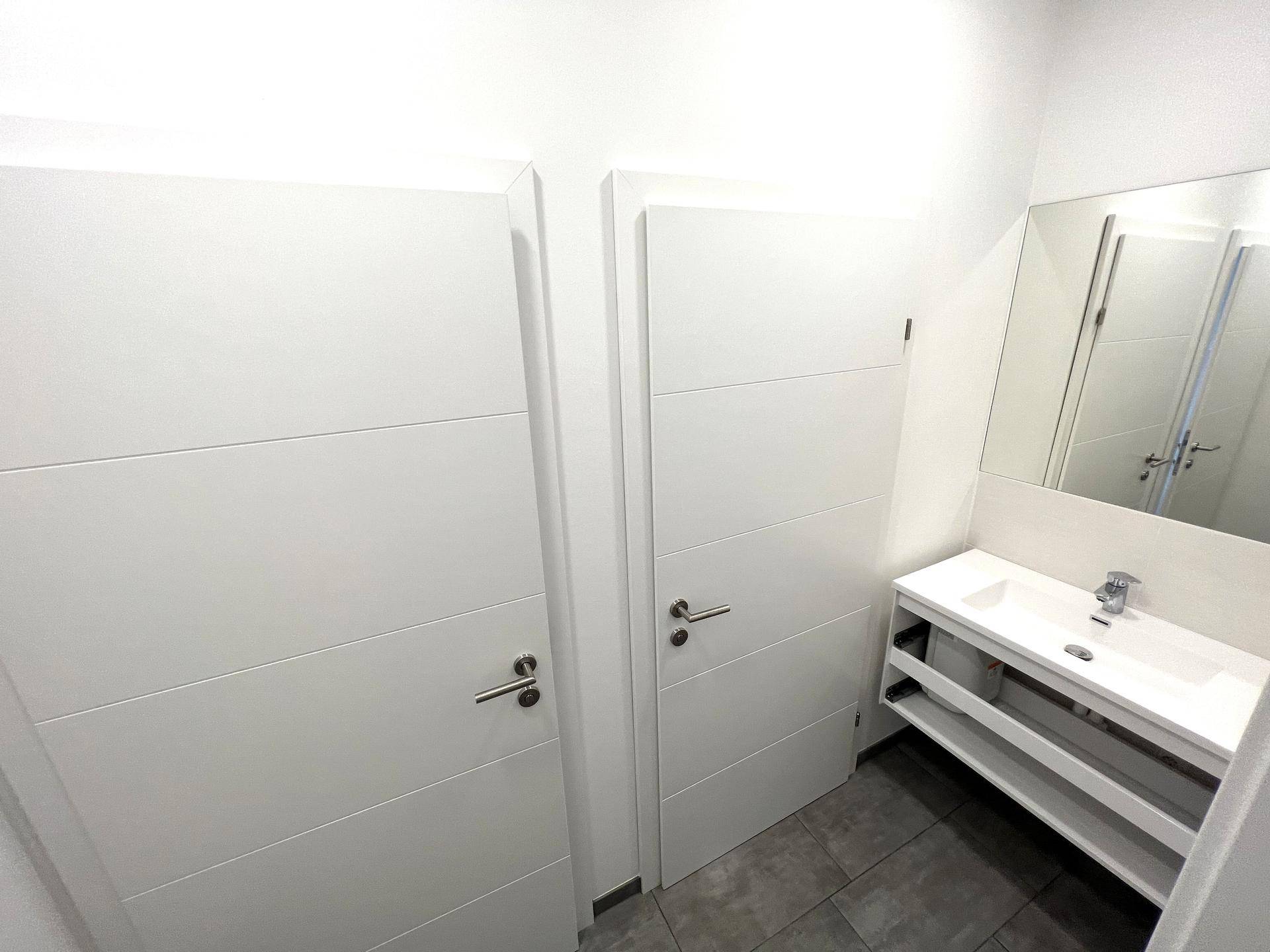 Heller Waschraum mit modernen Waschtischen und Spiegeln, angrenzend an separate Toilettenkabinen.