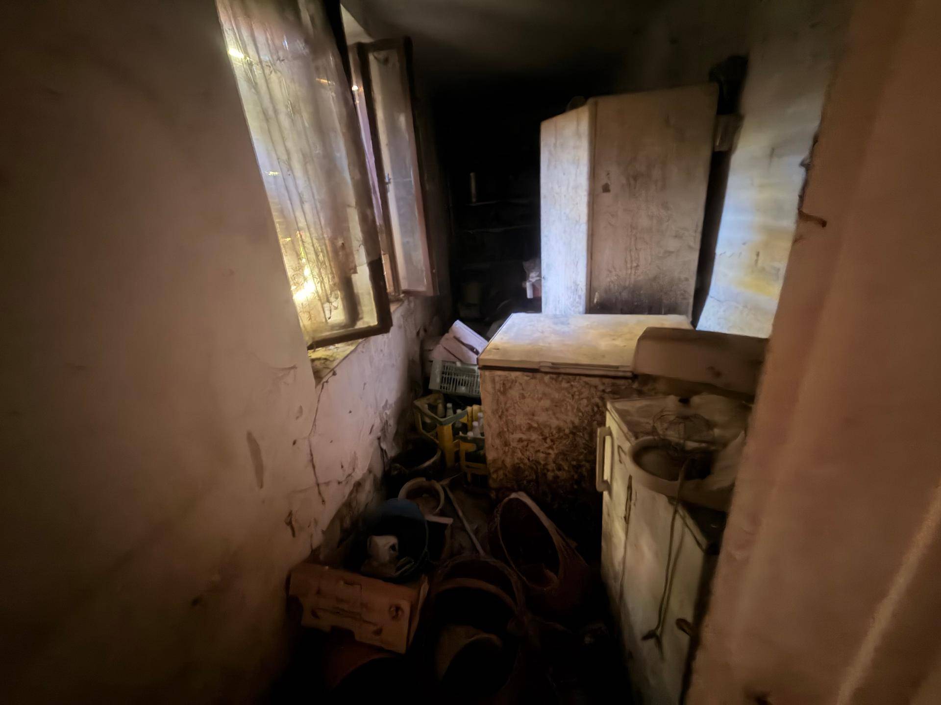 Dunkler Abstellraum mit alten Geräten und Unordnung, durch ein Fenster beleuchtet.