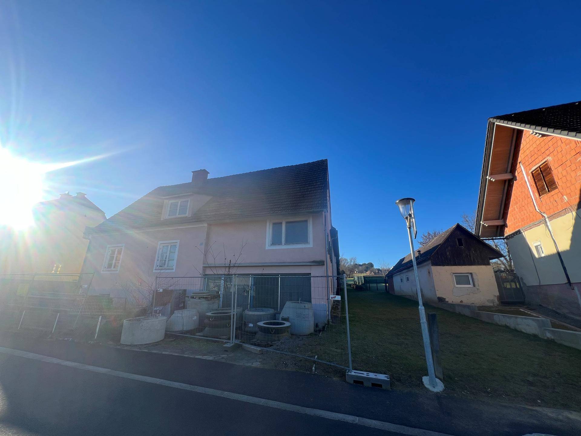 Weitwinkelaufnahme des rosa Hauses mit sonnigem Himmel und angrenzendem Grundstück.