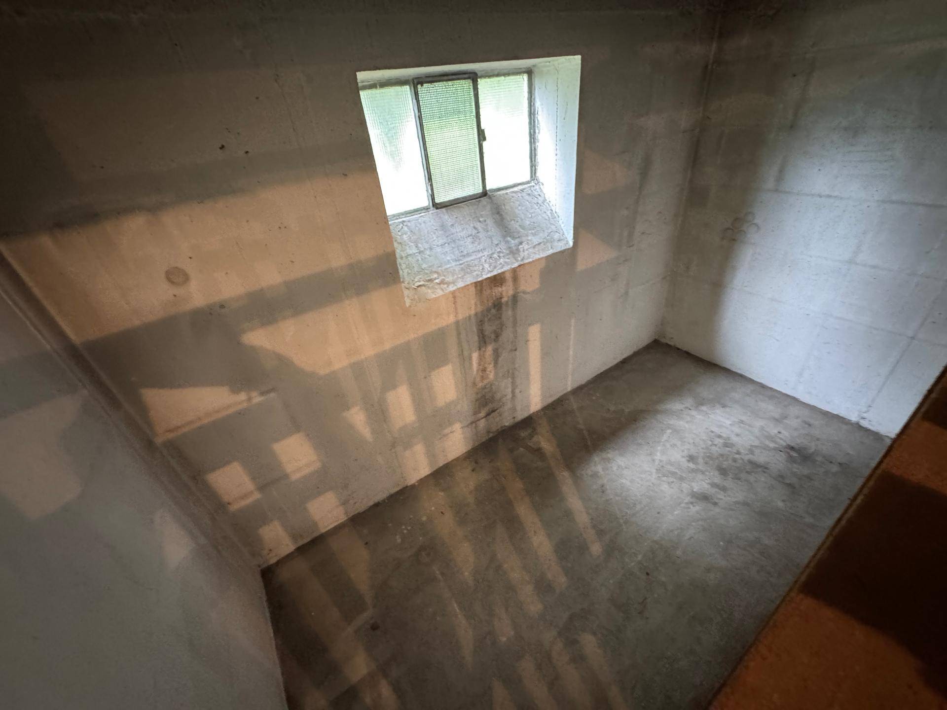 Unausgebauter Kellerraum mit kleinem Fenster, Betonwänden und -boden.