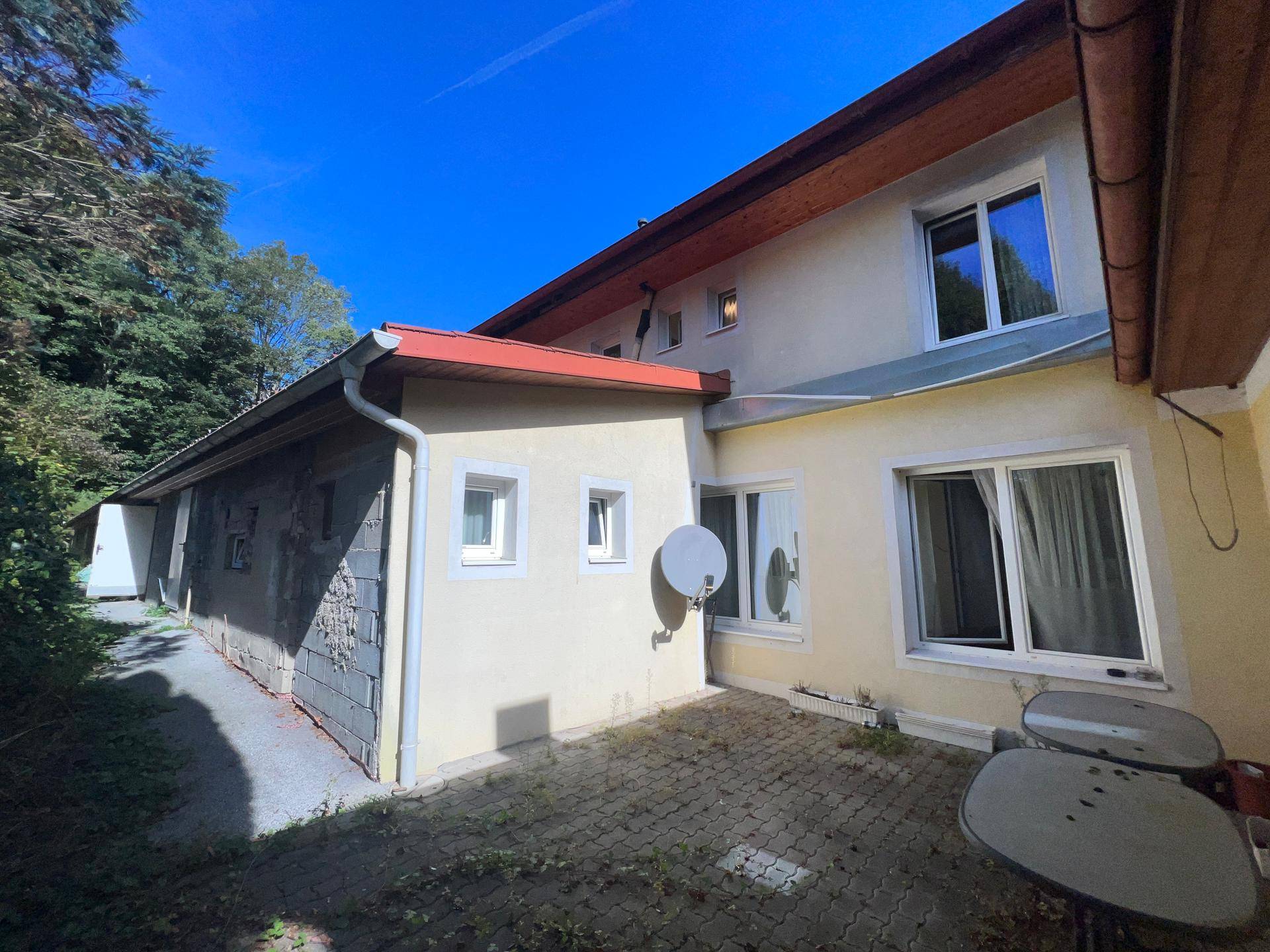 Kleine gepflasterte Terrasse hinter dem Gebäude mit einfachen Gartenmöbeln und Blick ins Grüne.