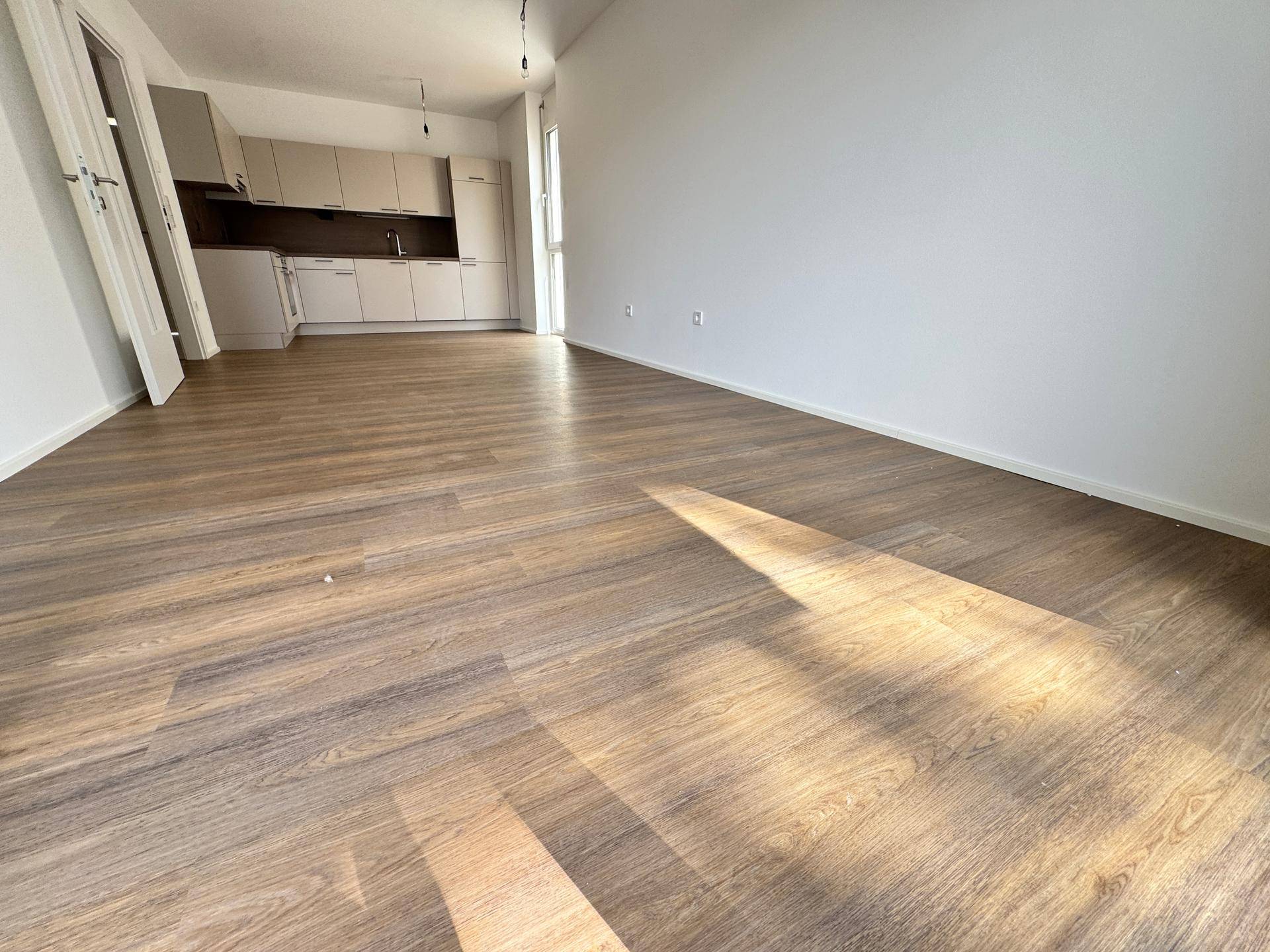 Geräumiger, heller Wohnbereich mit Laminatboden und einer modernen Küche im Hintergrund.