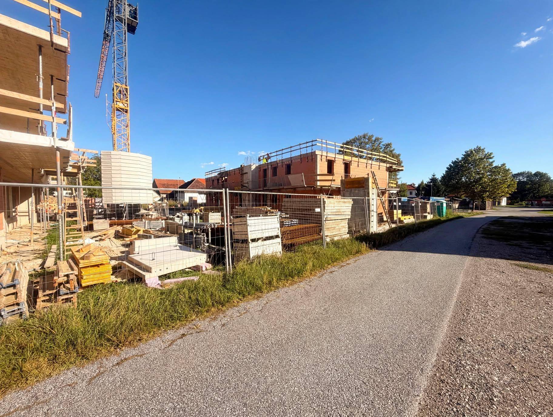 Weitläufige Baustelle mit Kran, Rohbauten und Baumaterialien entlang eines Feldweges.