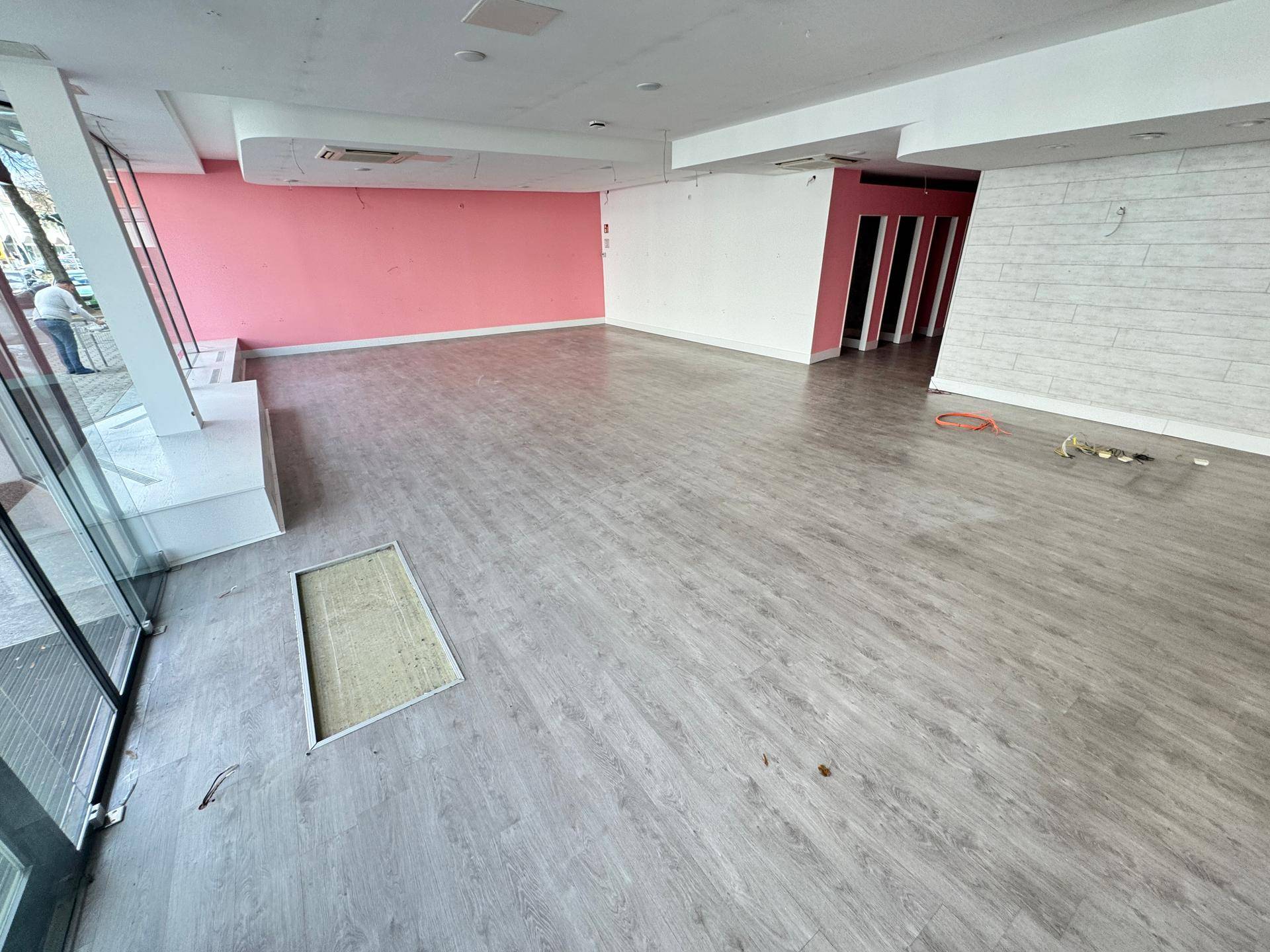 Geräumiger Verkaufsraum mit Laminatboden, rosa Wänden und Blick auf den Eingangsbereich.