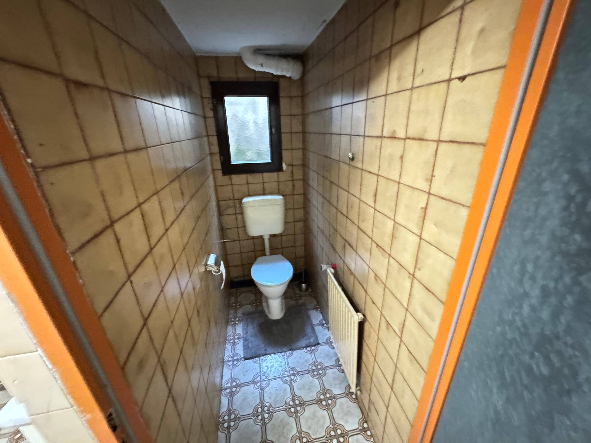 Kleines Gäste-WC mit braunen Fliesen, Toilette und einem Fenster für natürliche Belüftung.