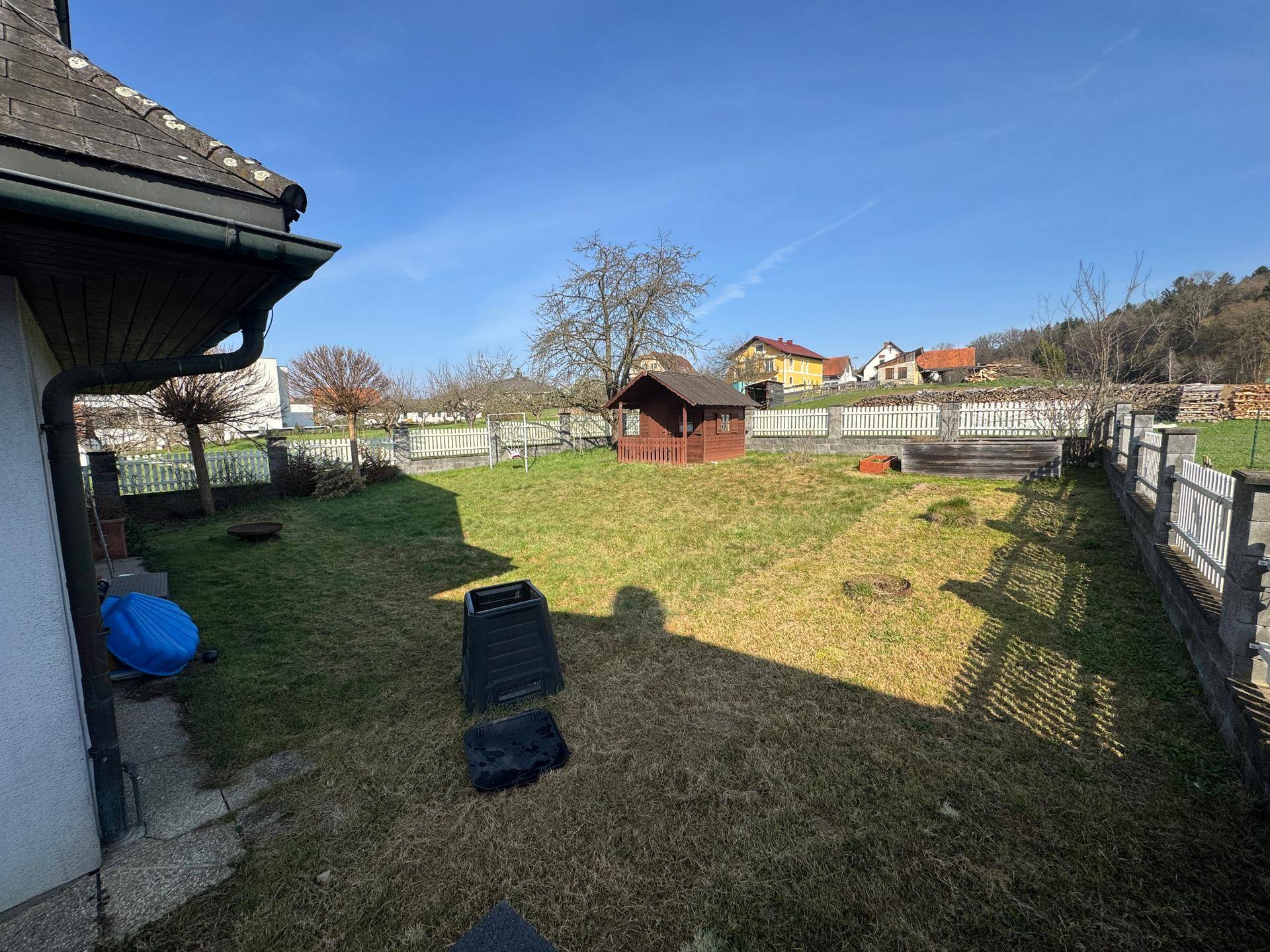 Sonniger Garten mit Rasen, einem kleinen Schuppen und Blick auf die umliegende Landschaft.